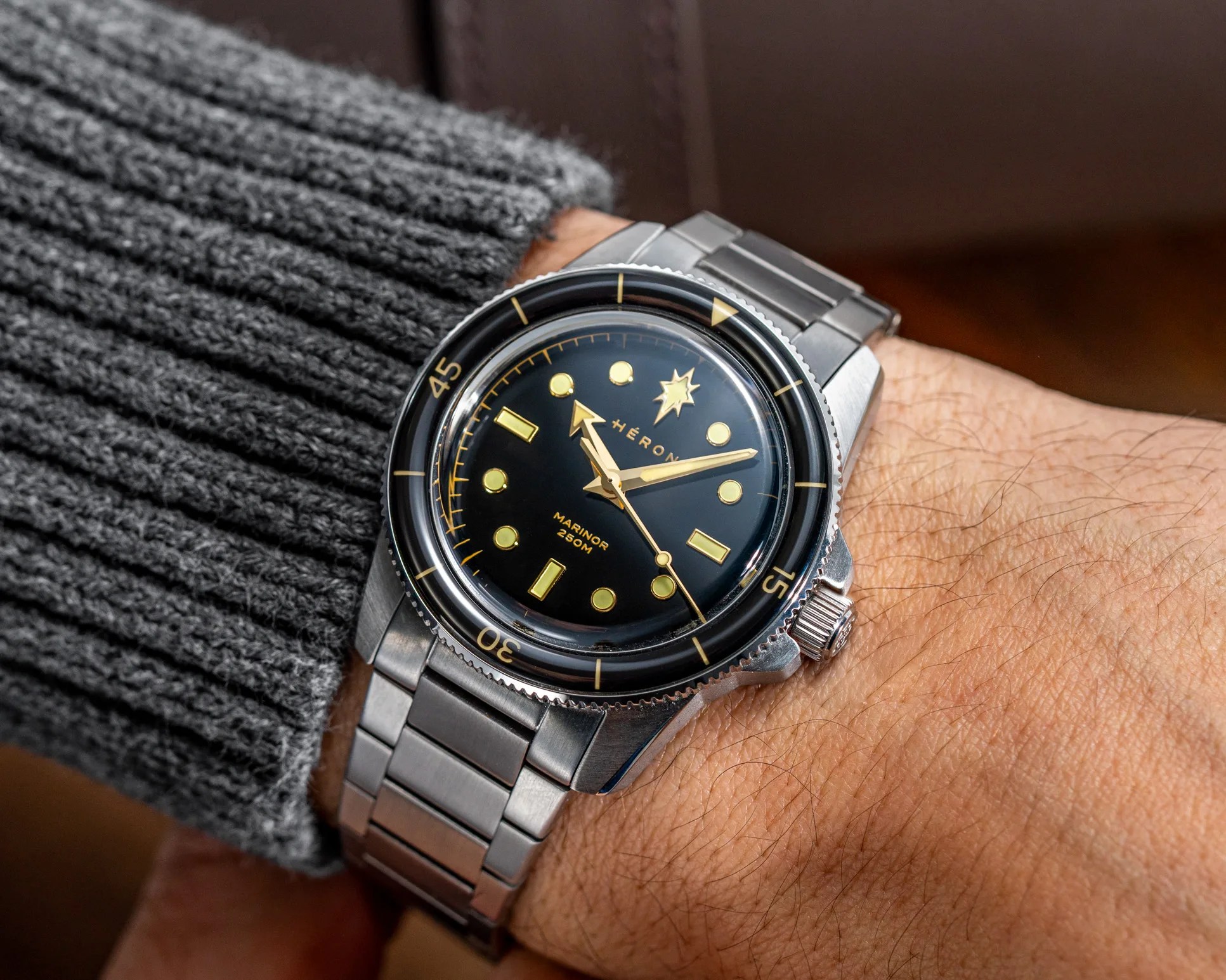 Silver metal wristwatch with black dial and gold markers worn on a wrist with a gray knitted sleeve.
