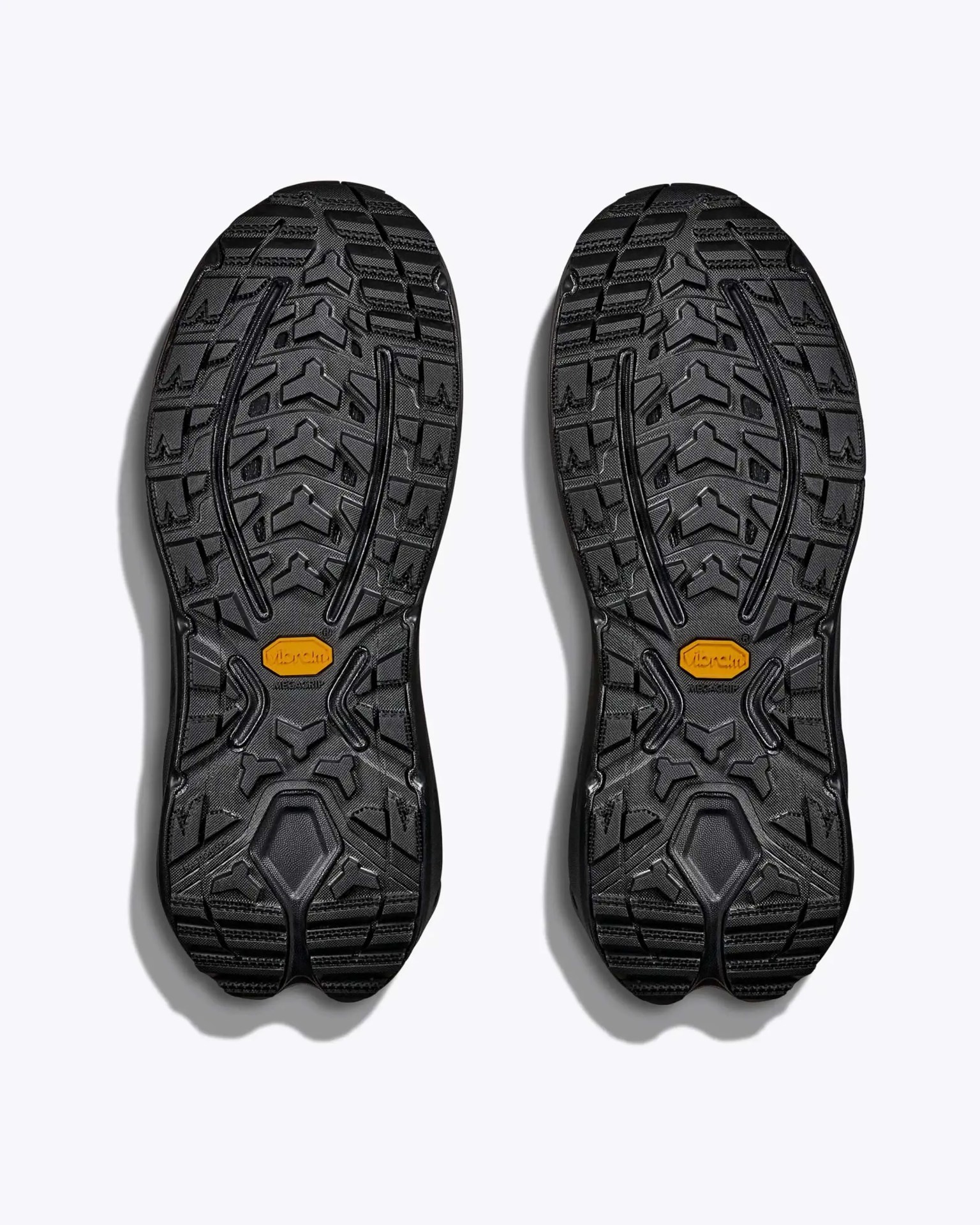 Pair of black rubber shoe soles with deep treads and orange Vibram logo in the center.