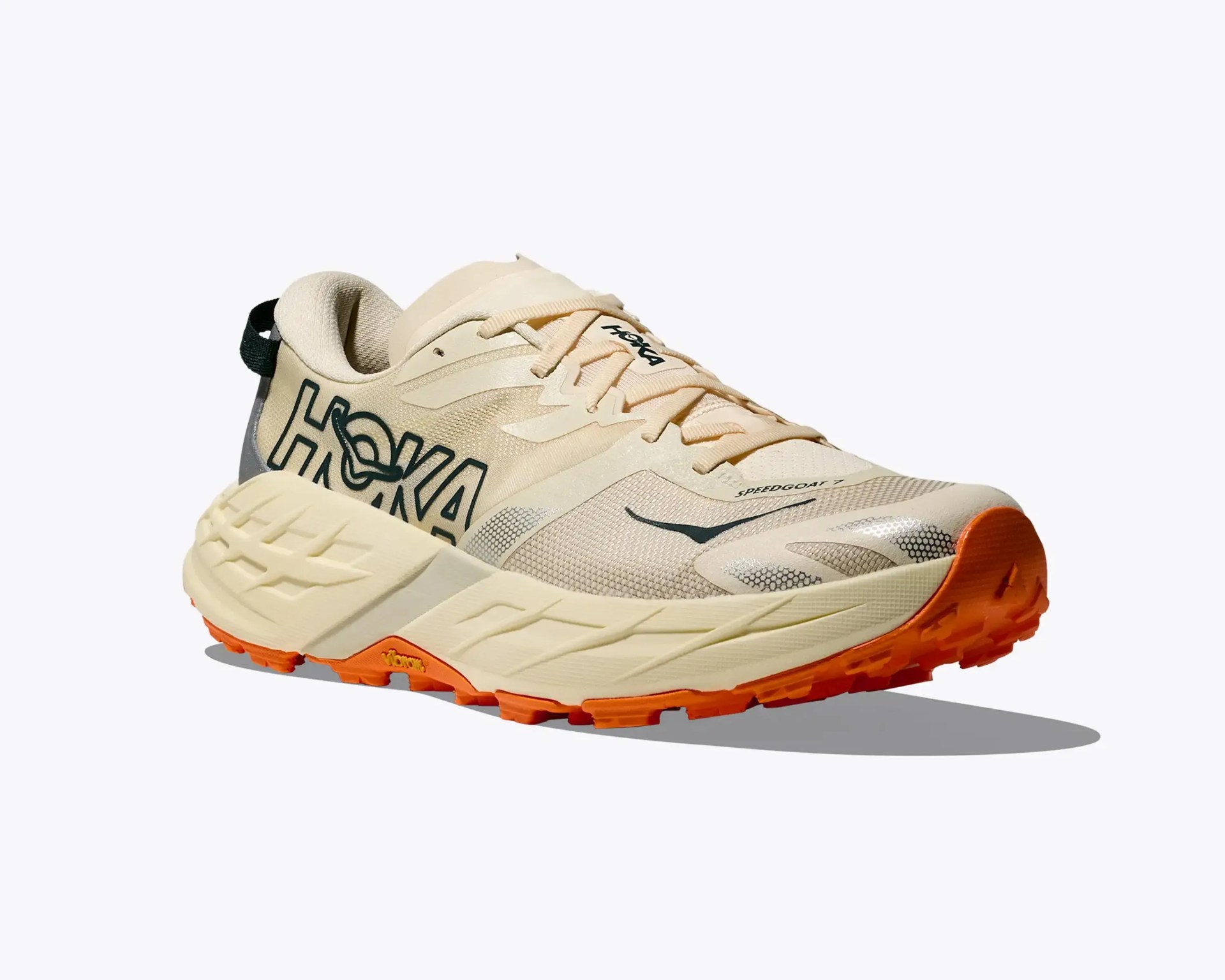Beige Hoka Speedgoat 7 trail running shoe with orange Vibram sole and black logo on the side.