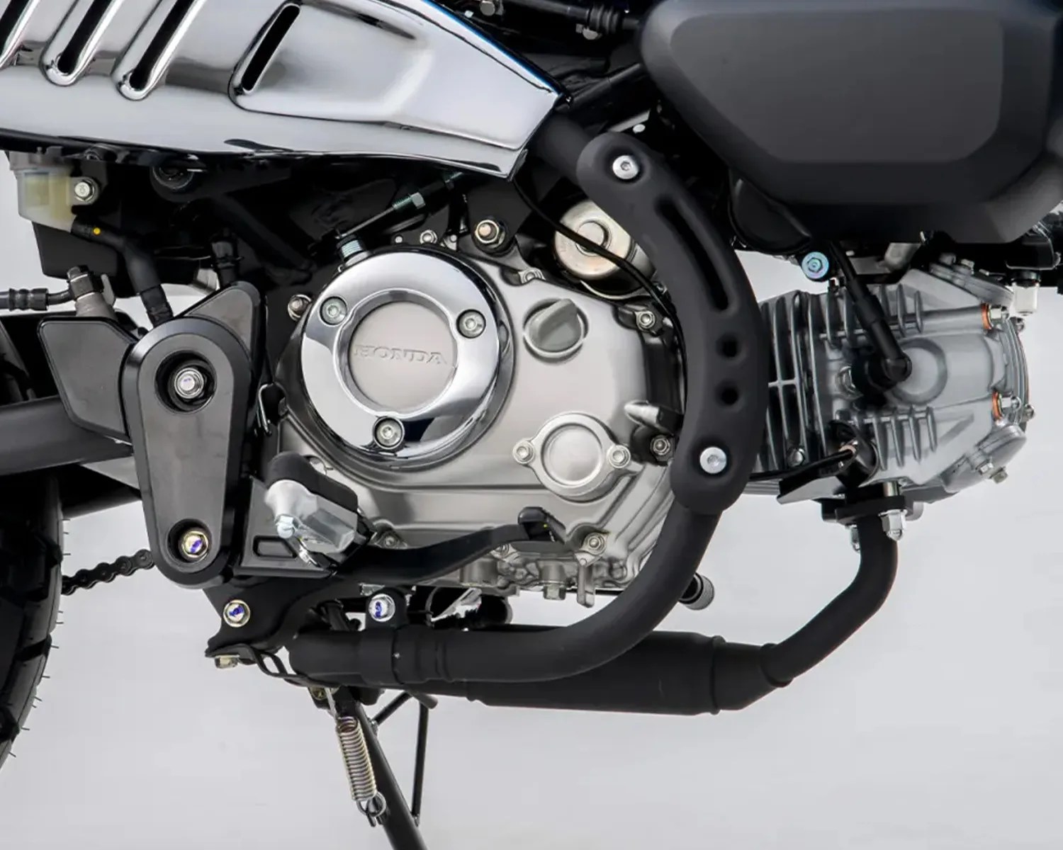 Close-up of a silver Honda motorcycle engine with black exhaust pipes and foot pedal.