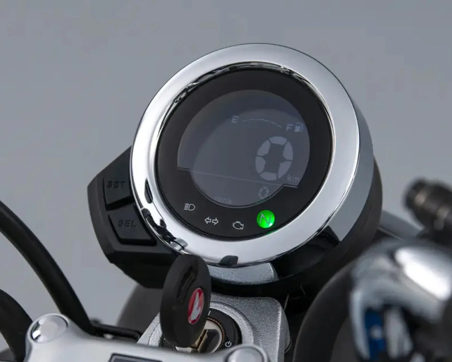 Round digital motorcycle speedometer with chrome bezel and green indicator light.