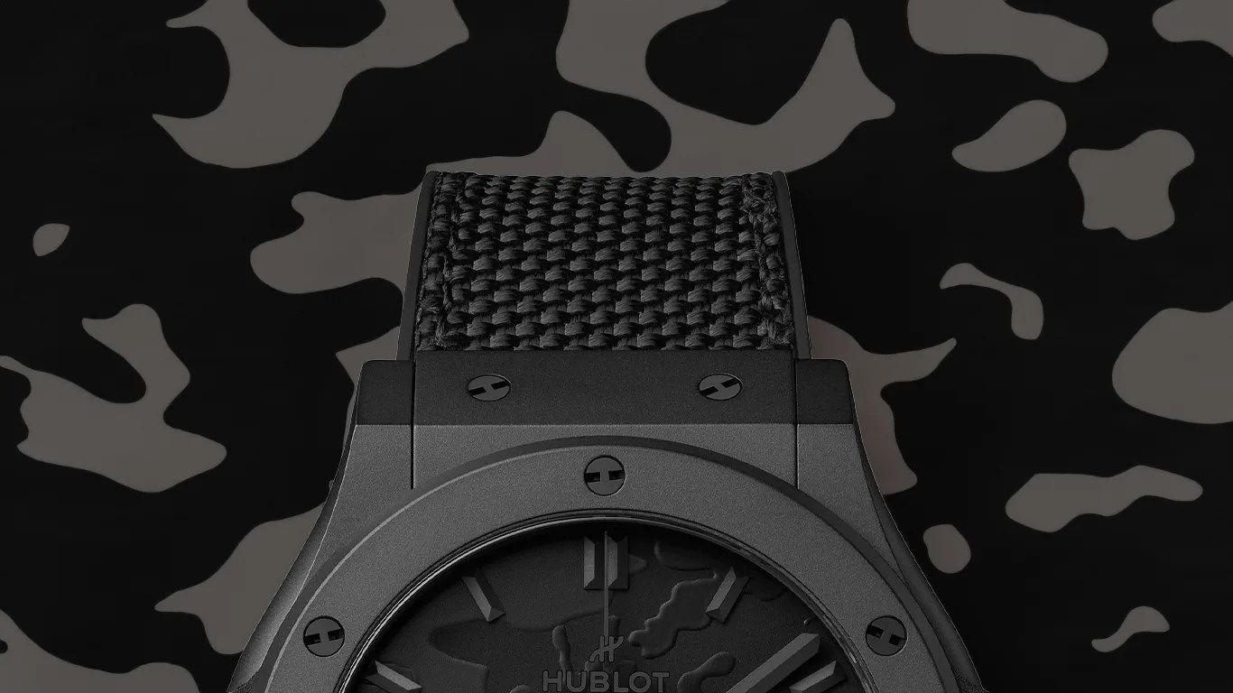 Black Hublot watch with textured strap and camouflage-patterned dial on matching camo background.