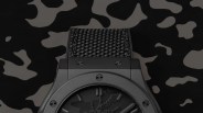 Black Hublot watch with textured strap and camouflage-patterned dial on matching camo background.