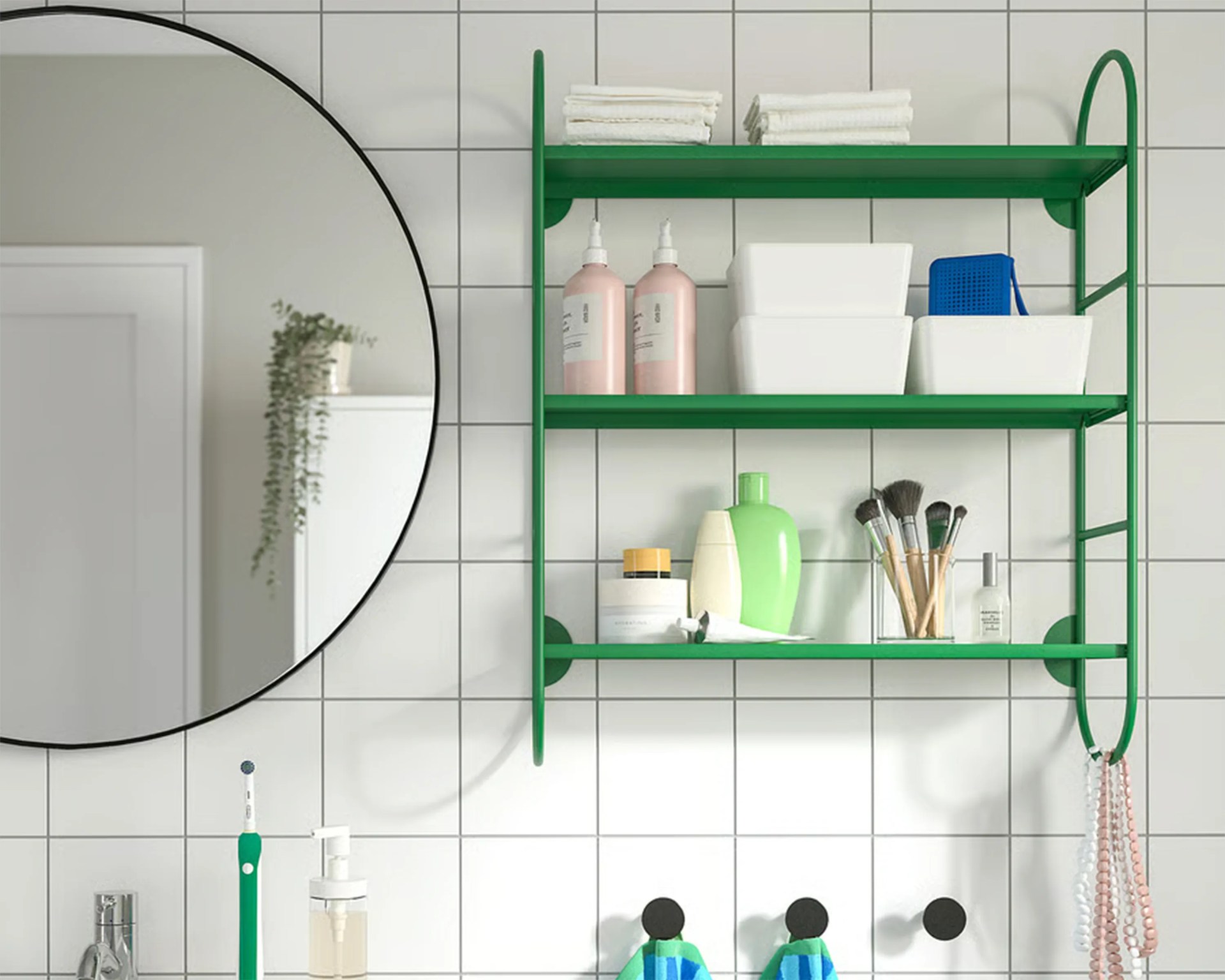 Green metal wall shelf with toiletries and makeup brushes mounted on white tiled bathroom wall next to a round mirror.