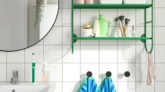Green wall-mounted shelf with toiletries and makeup brushes above a white tiled bathroom sink with a green and white electric toothbrush.