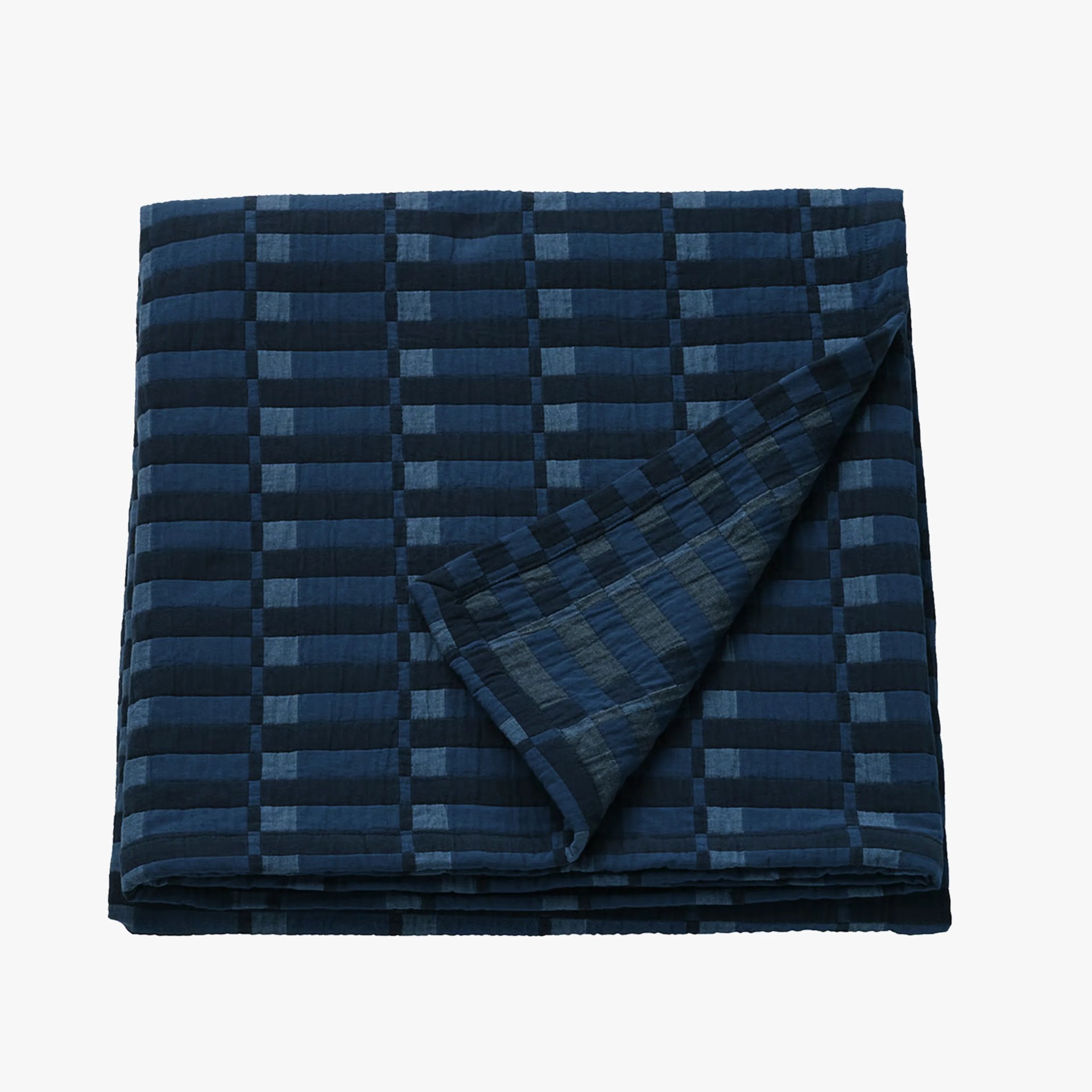 Folded dark blue quilt with a checkered pattern and one corner flipped over.