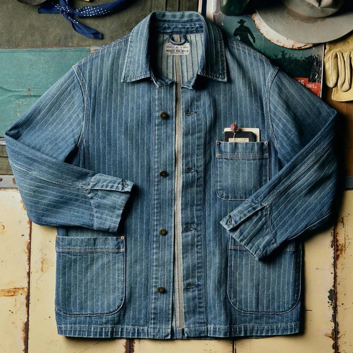 Blue pinstriped denim chore jacket with three front pockets, buttons, and a collar laid flat.