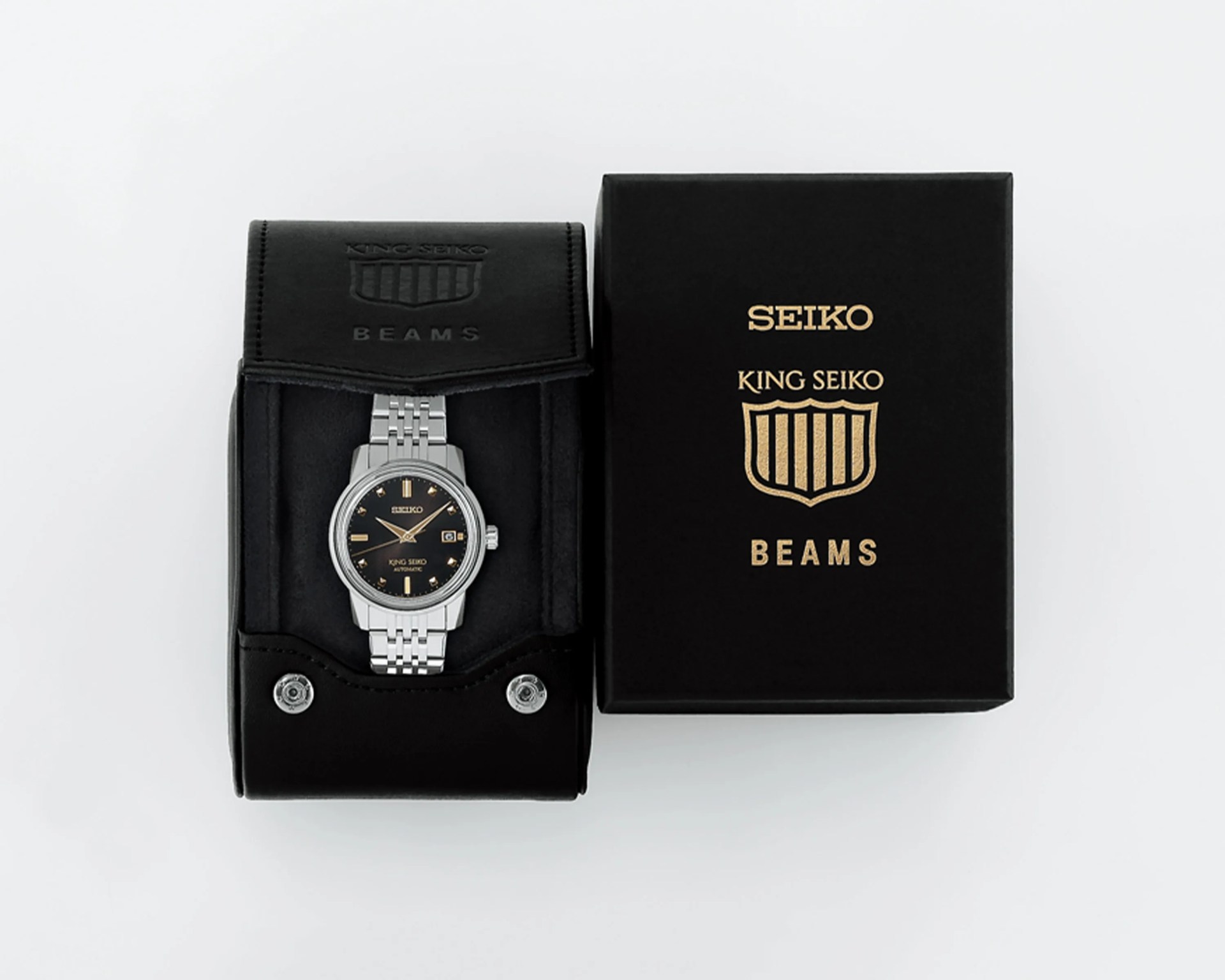 Silver Seiko King Seiko automatic watch with black dial and gold markers in black leather case next to black box with gold logo.