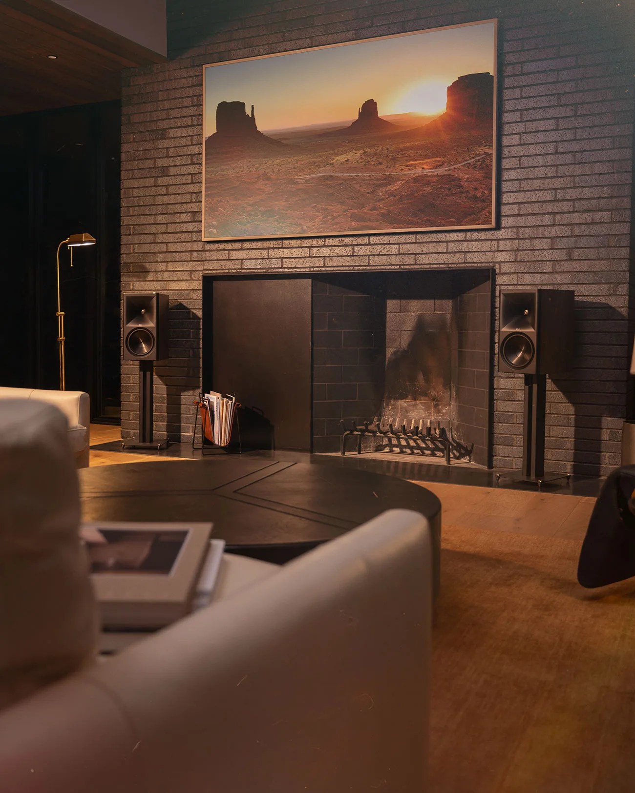 Modern living room with black brick fireplace, two black speakers on stands, and a landscape photo above.
