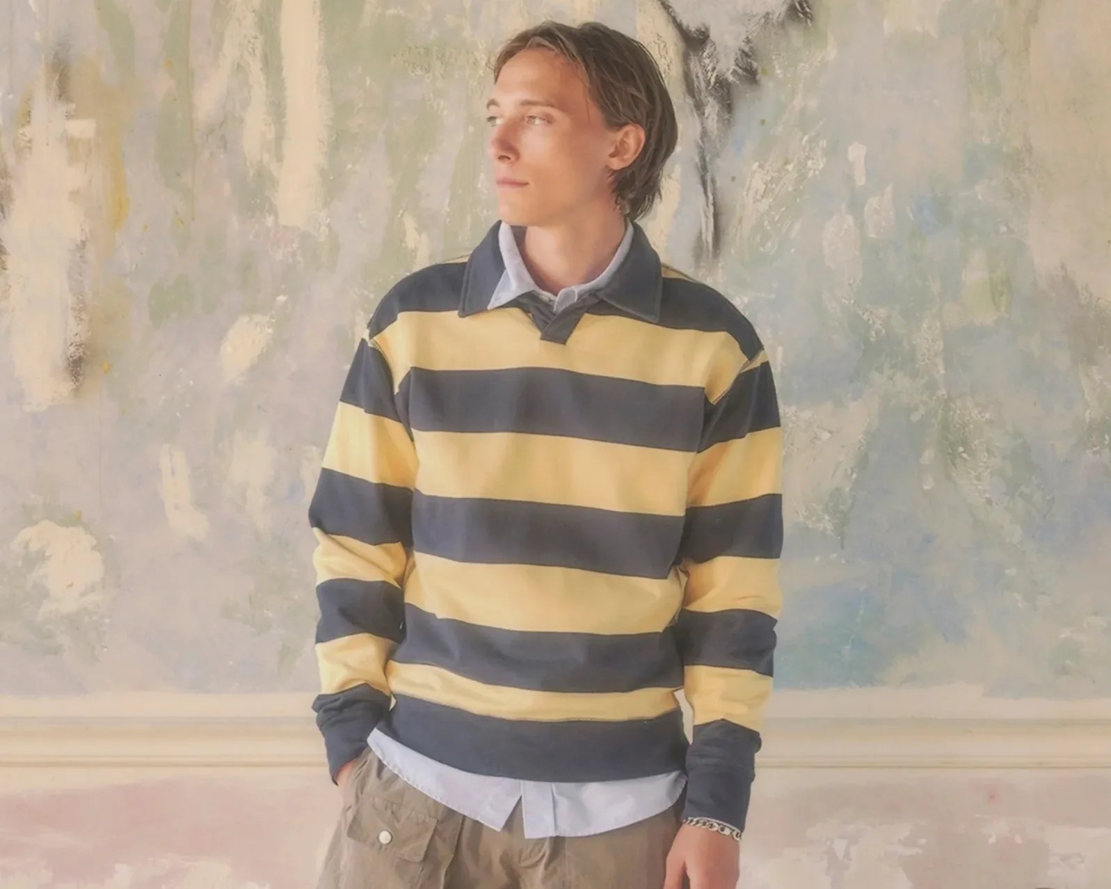 Person wearing a yellow and navy blue striped rugby shirt over a light blue button-up shirt.
