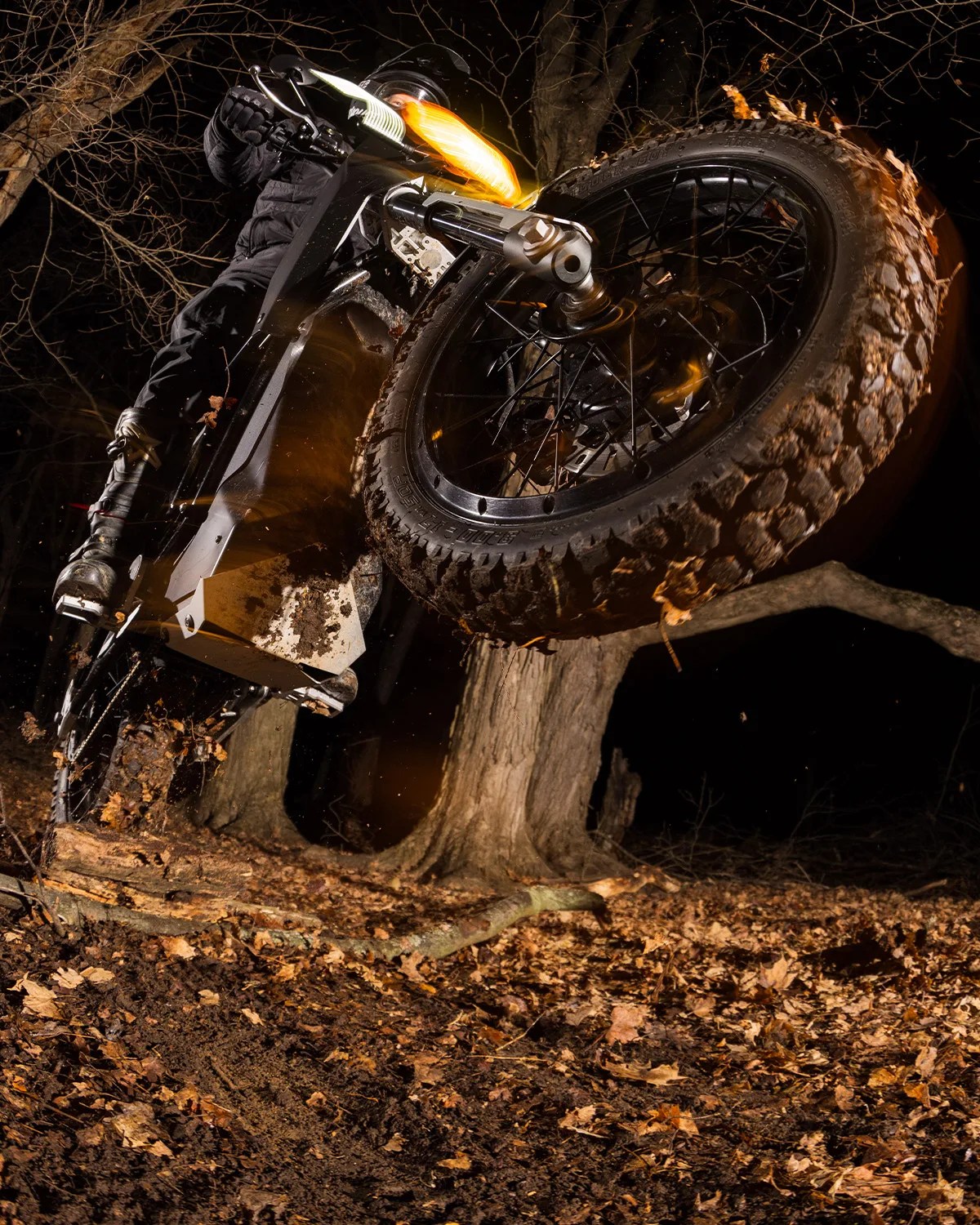 Electric dirt bike with knobby tires kicking up leaves in a dark forest at night.