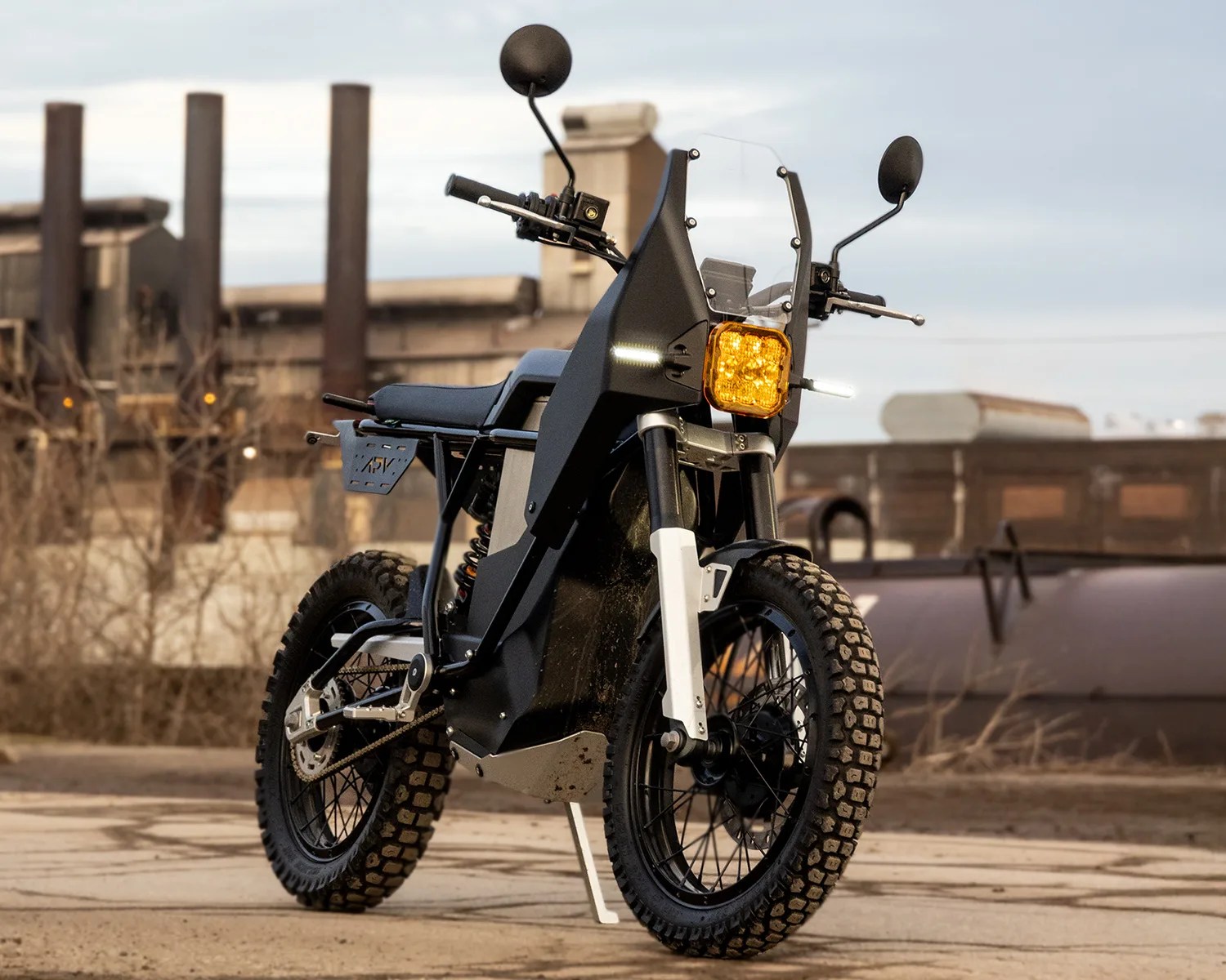 Black and white off-road electric motorcycle with knobby tires and square amber headlight parked on a concrete surface.