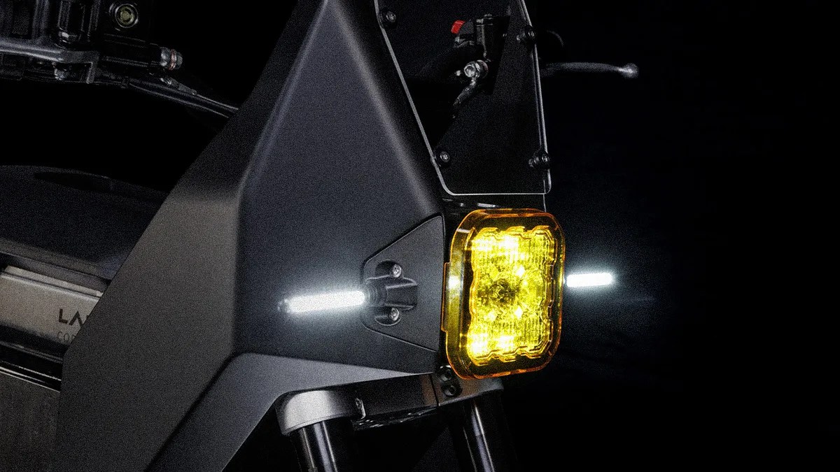Close-up of a black electric motorcycle front with a yellow headlight and white LED side lights against a dark background.