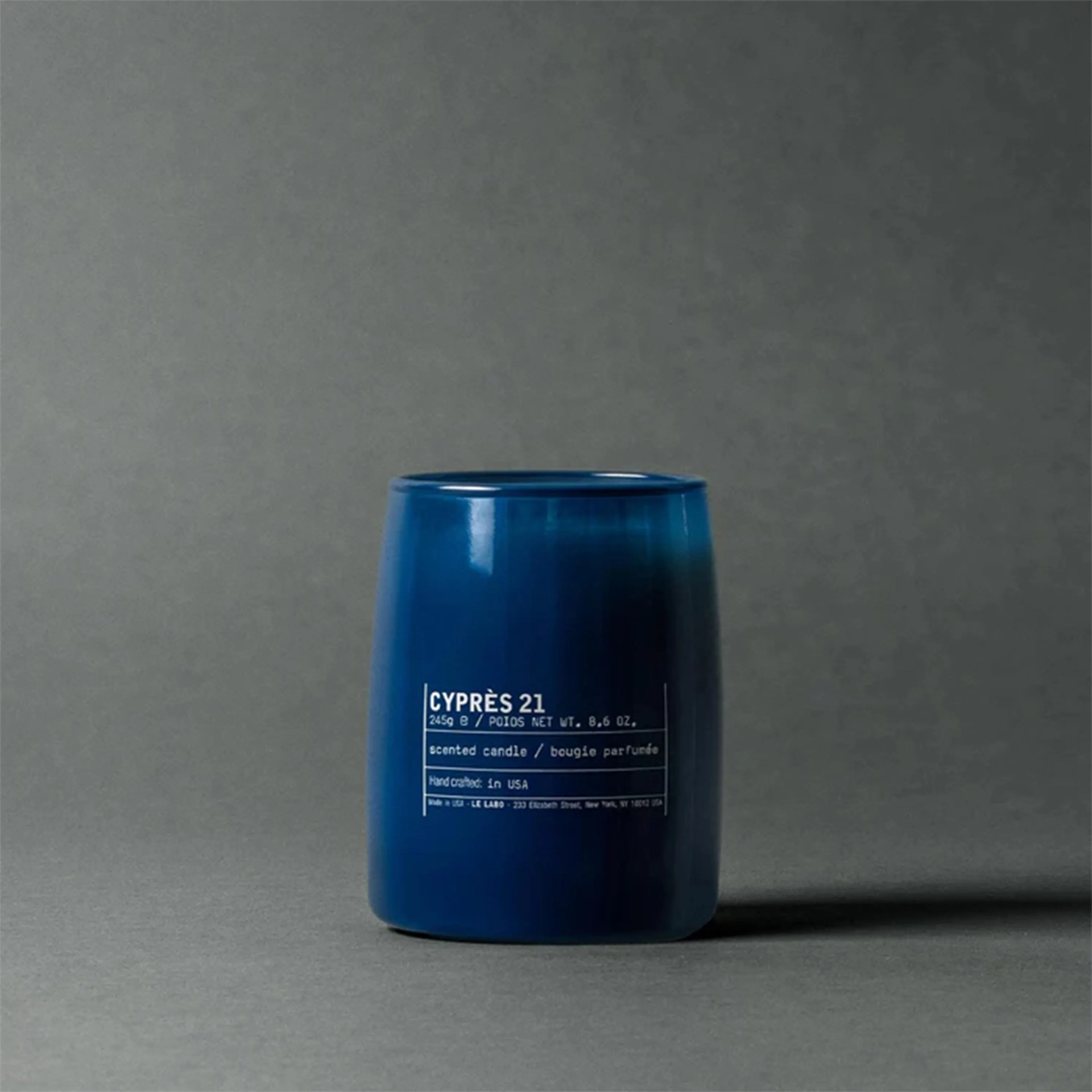 Blue glass candle holder with white text labeled "Cypr&egrave;s 21" on a gray surface.