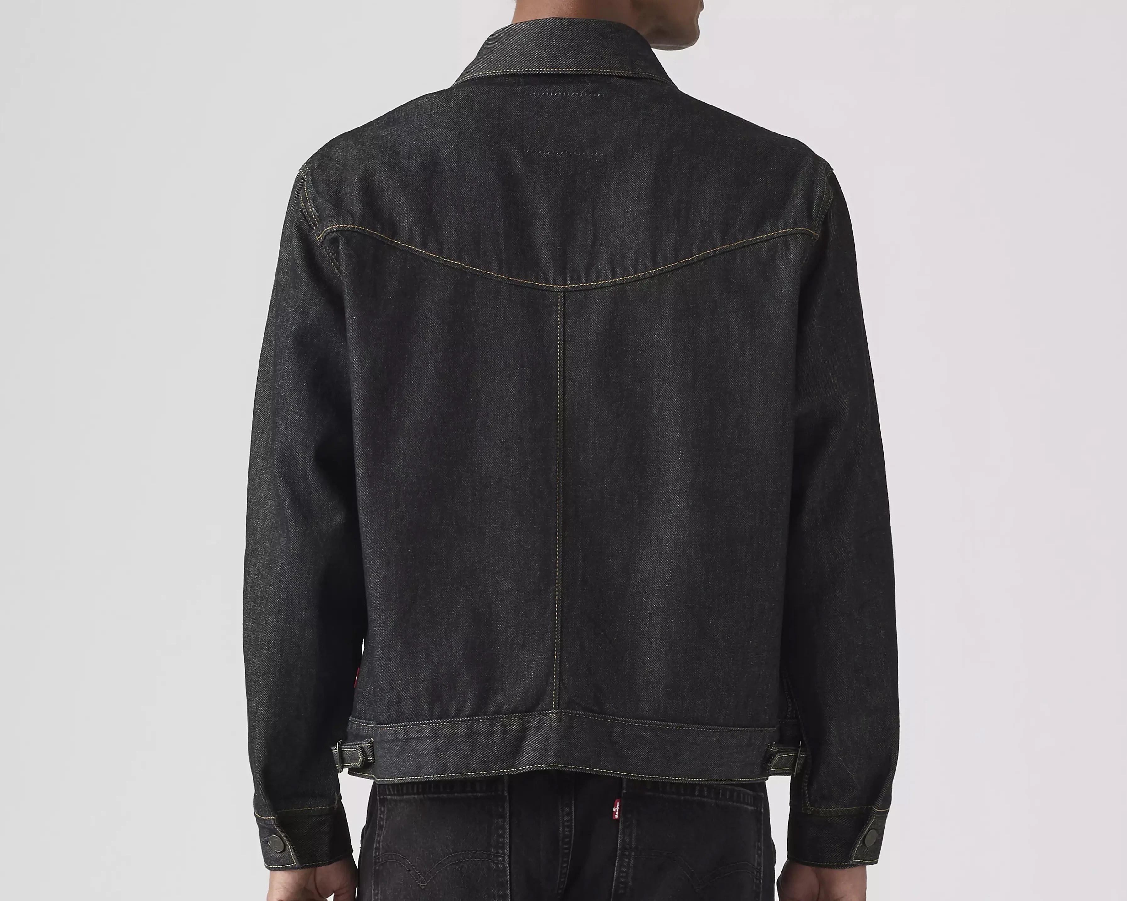 Back view of a person wearing a black denim jacket with yellow stitching and adjustable side tabs.