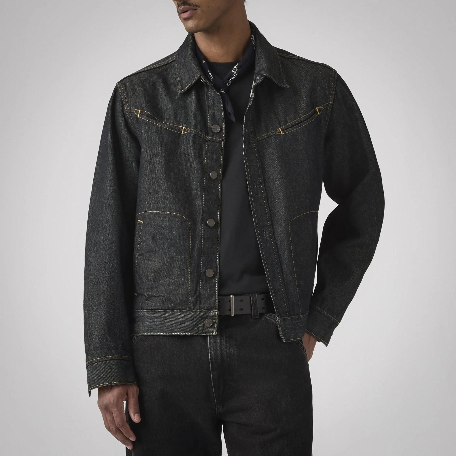 Black denim jacket with yellow stitching worn over a black shirt and paired with black jeans.