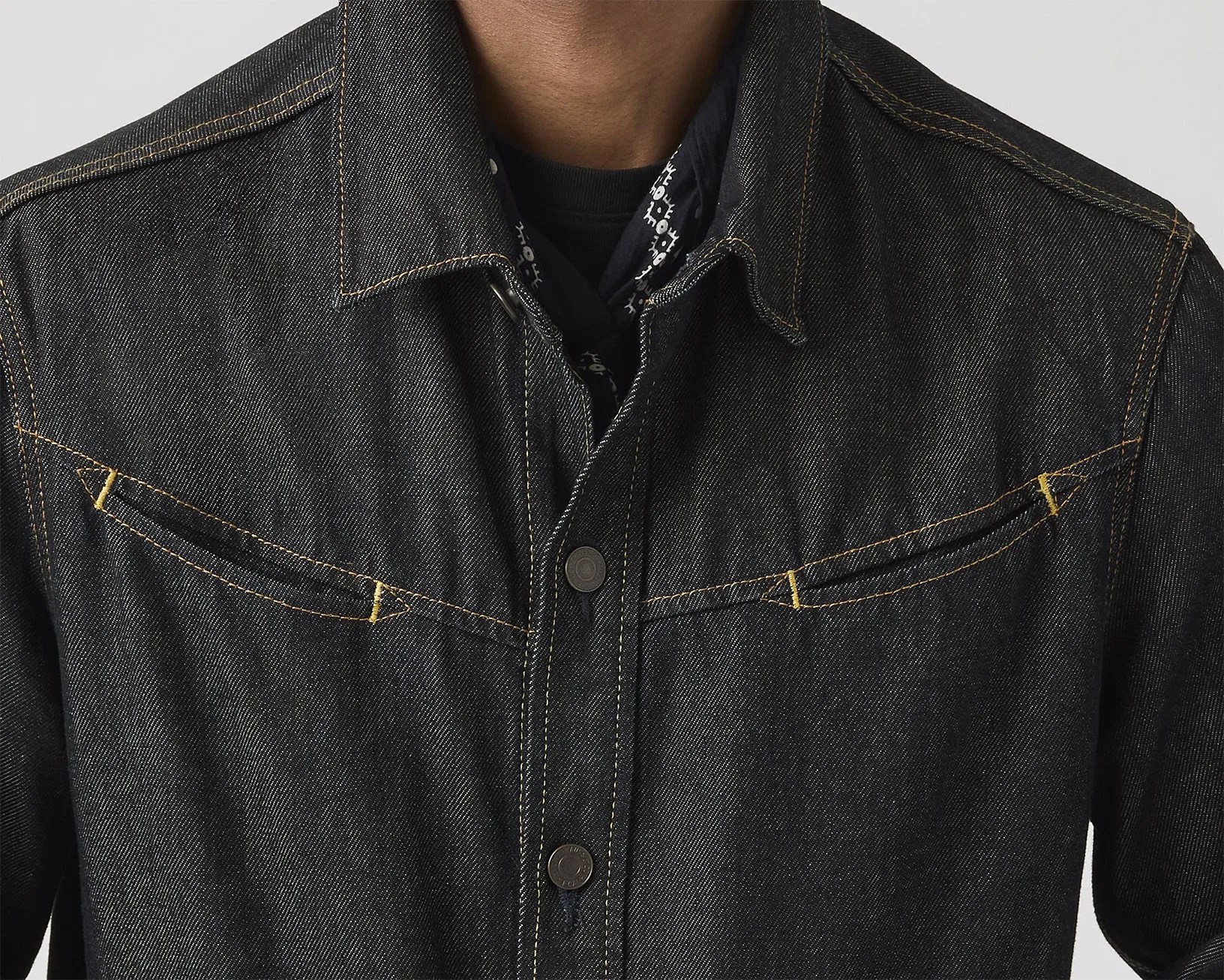Close-up of a black denim jacket with yellow stitching and metal snap buttons.