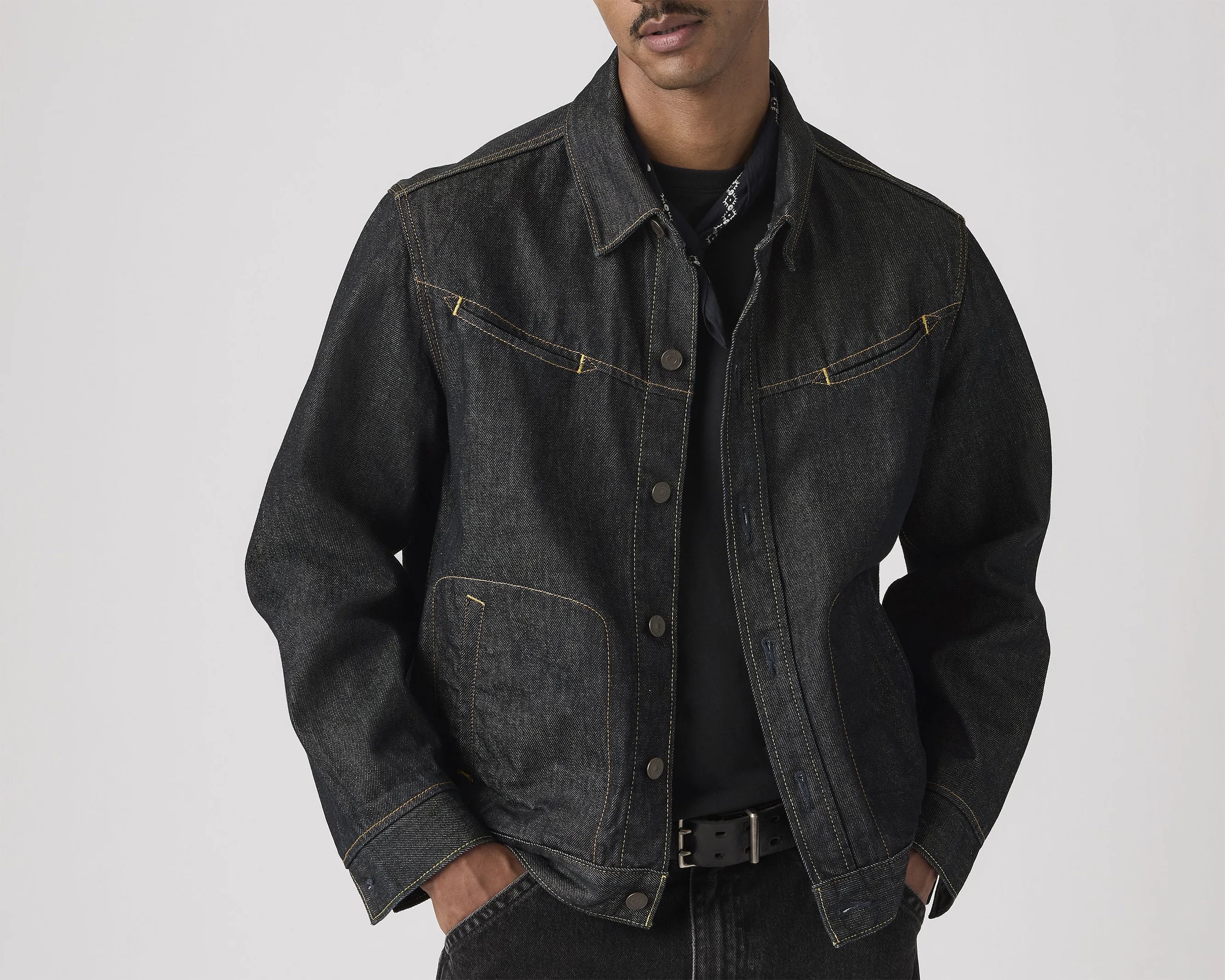 Black denim jacket with yellow stitching worn over a black shirt and paired with black pants and belt.