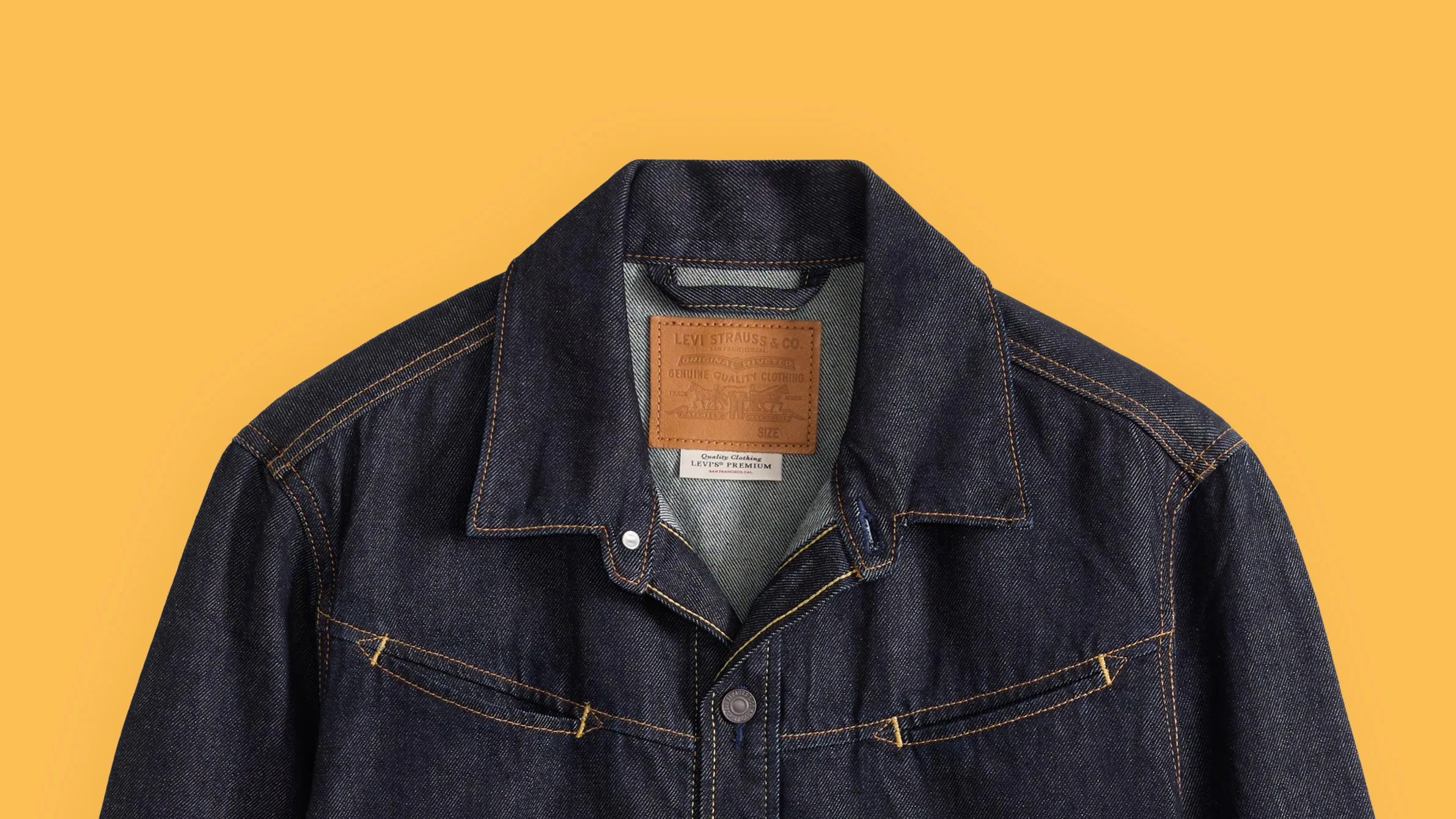 Dark indigo Levi's denim jacket with brown stitching and leather brand patch on a yellow background.
