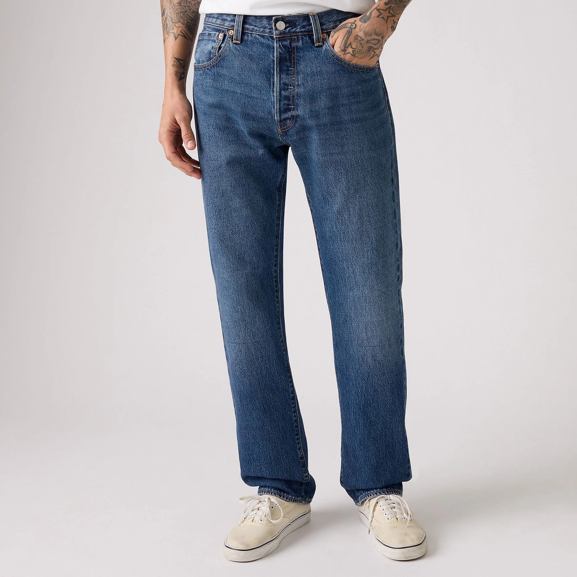 Straight-leg blue denim jeans worn with white sneakers and a white shirt, hands in pockets.