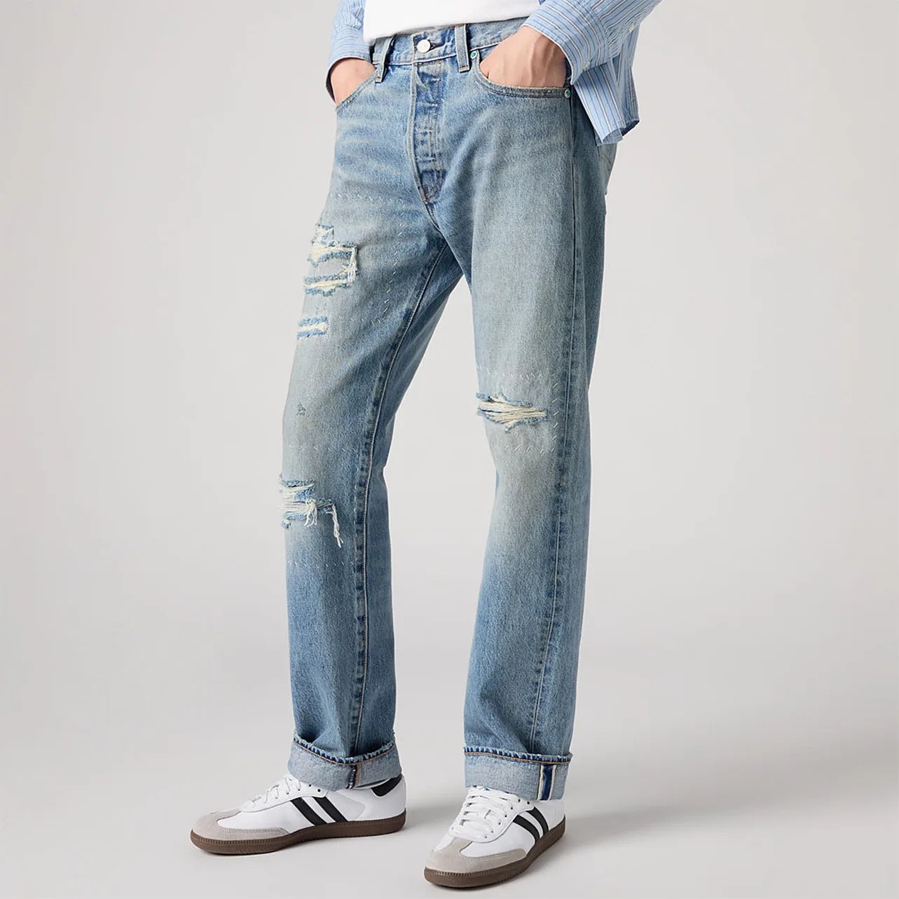 Light blue distressed straight-leg jeans with rolled cuffs worn with white sneakers with black stripes.