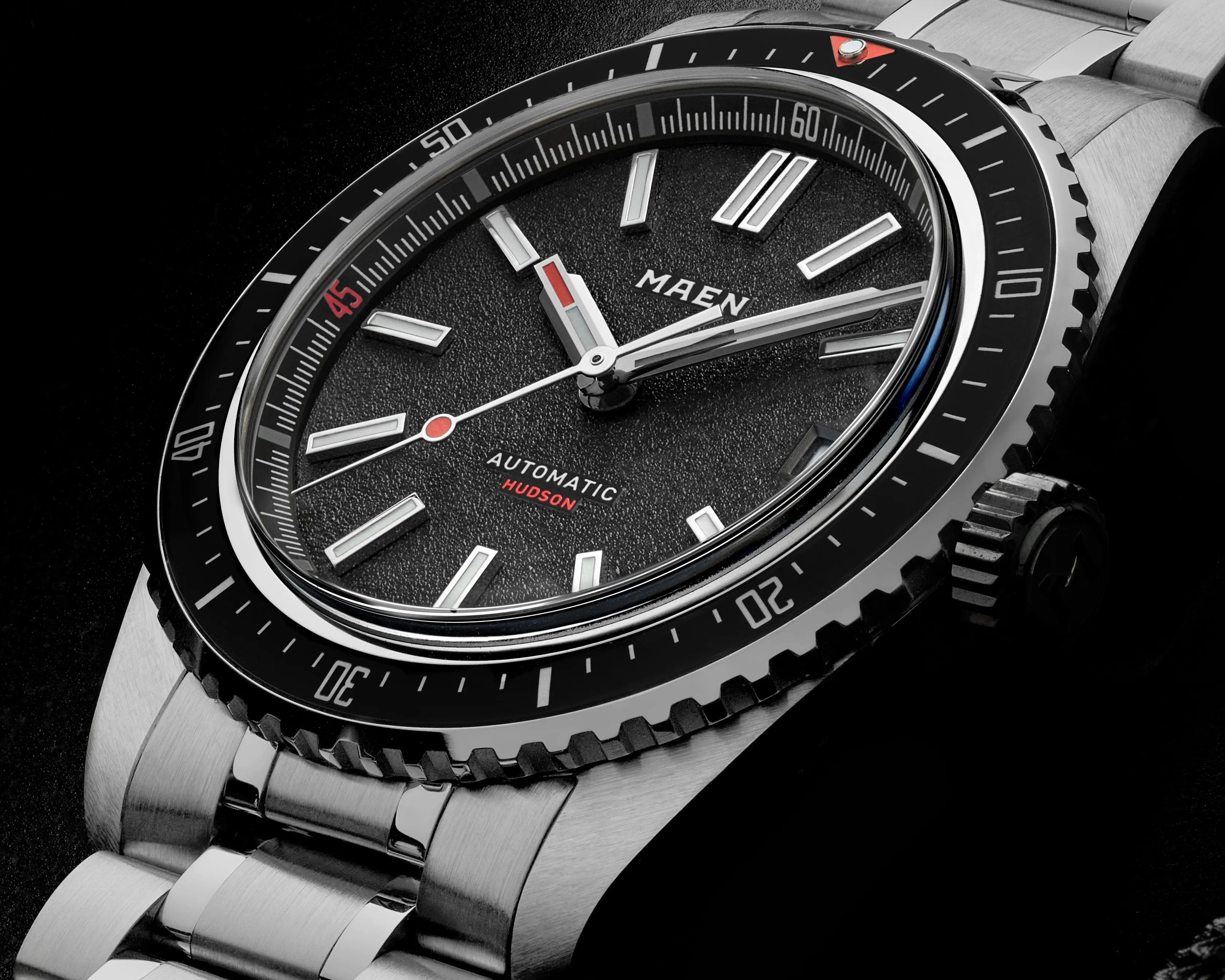 Close-up of a Maen Hudson automatic watch with a black textured dial, silver markers, and a stainless steel bracelet.