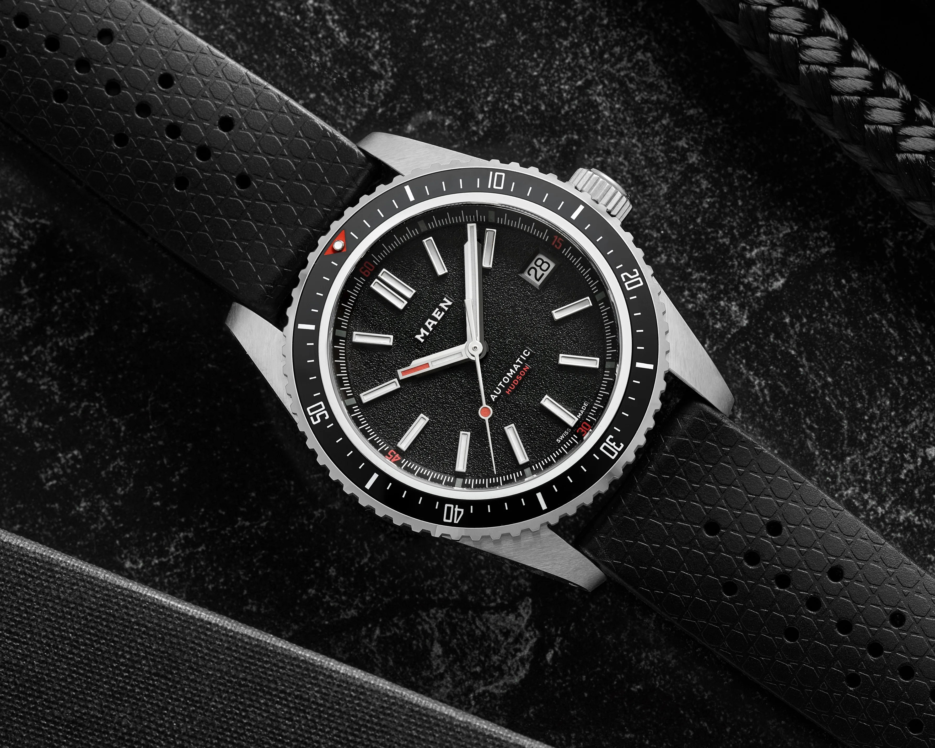 Black Maen Hudson automatic wristwatch with silver markers and a black textured rubber strap on a dark surface.