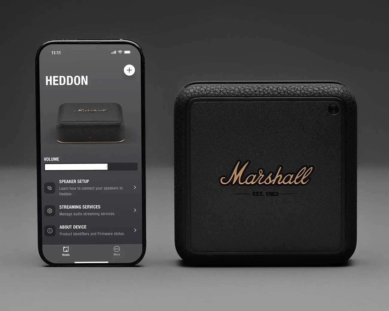 Black Marshall Heddon wireless speaker with textured finish next to a smartphone displaying its control app.