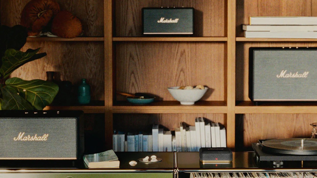 Three black Marshall speakers on a wooden shelf and cabinet with books, bowls, and a record player.