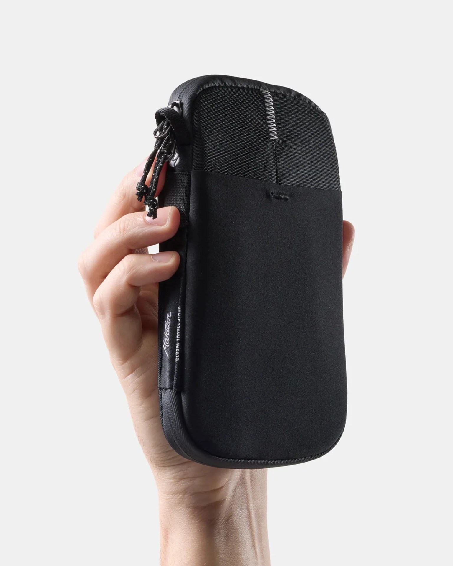 Hand holding a small black zippered pouch with a fabric loop and white stitching detail.