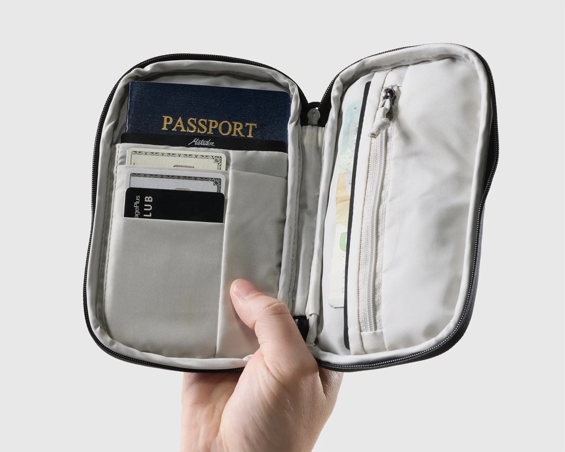 Light gray travel organizer with passport, cards, and cash held open in a hand against a plain background.