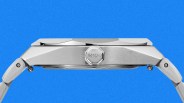 Side view of a silver stainless steel Mido watch case and bracelet against a blue background.