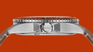Side view of a stainless steel Mido watch case with a ridged bezel and brown leather strap against an orange background.