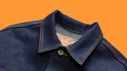 Dark blue denim jacket collar with orange stitching and a leather label featuring a face illustration.