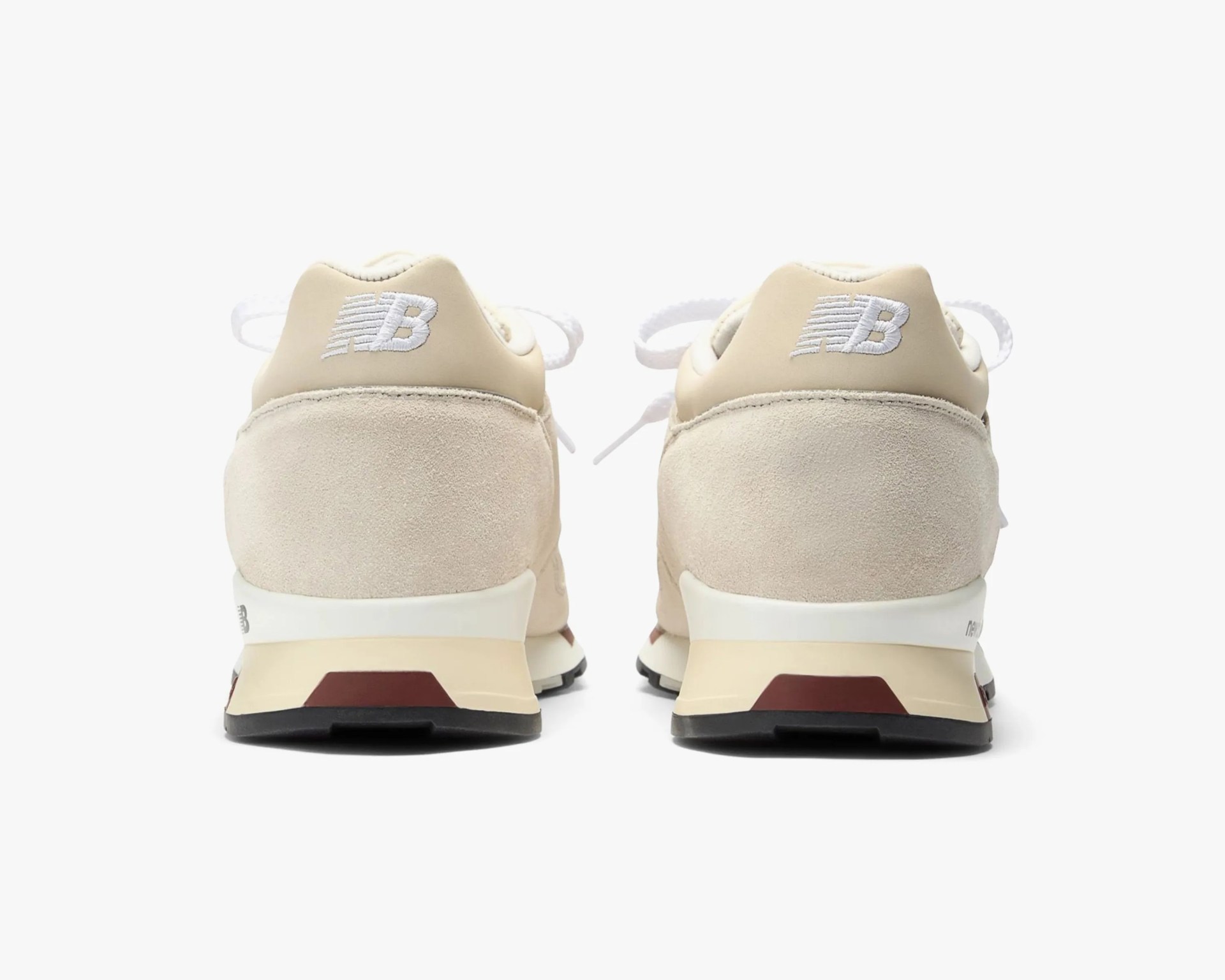 Pair of beige New Balance sneakers shown from the back with white embroidered logo and black soles.