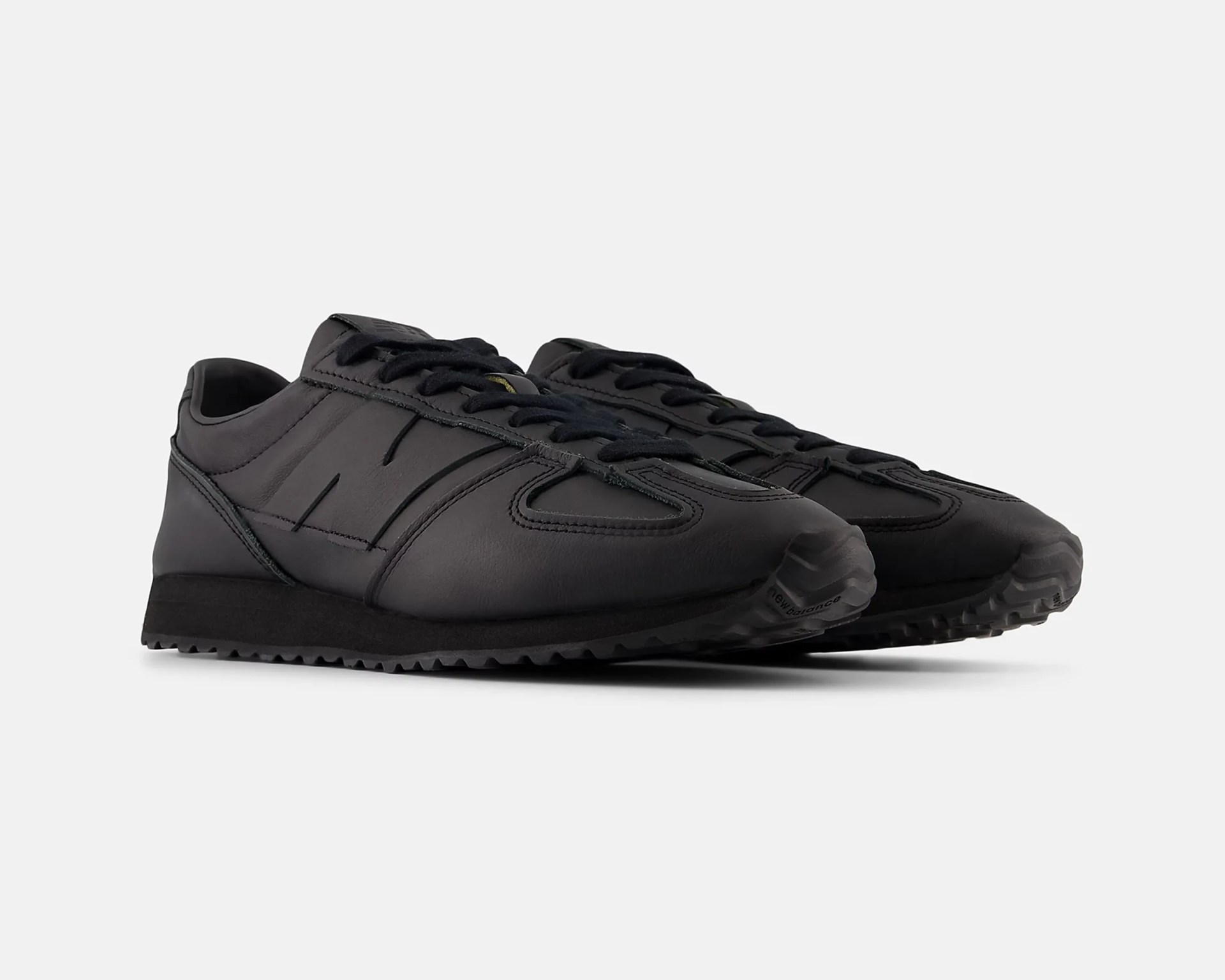 Pair of black leather sneakers with black laces and textured black rubber soles.