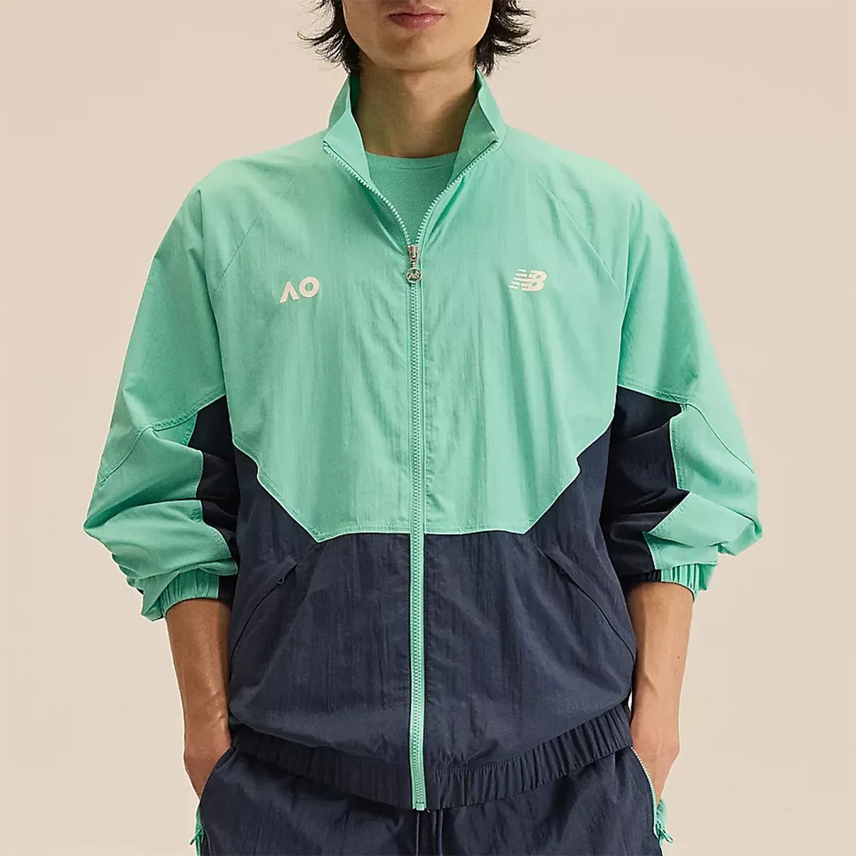 Two-tone mint green and navy blue zip-up sports jacket with logos on the chest worn by a person.