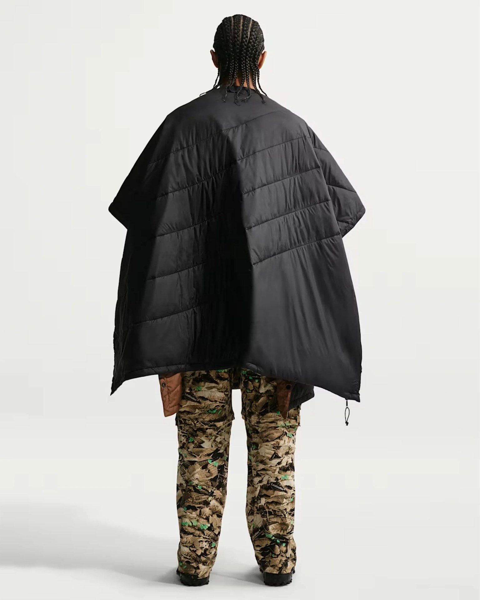 Person wearing a black quilted cape and camouflage pants, shown from the back.