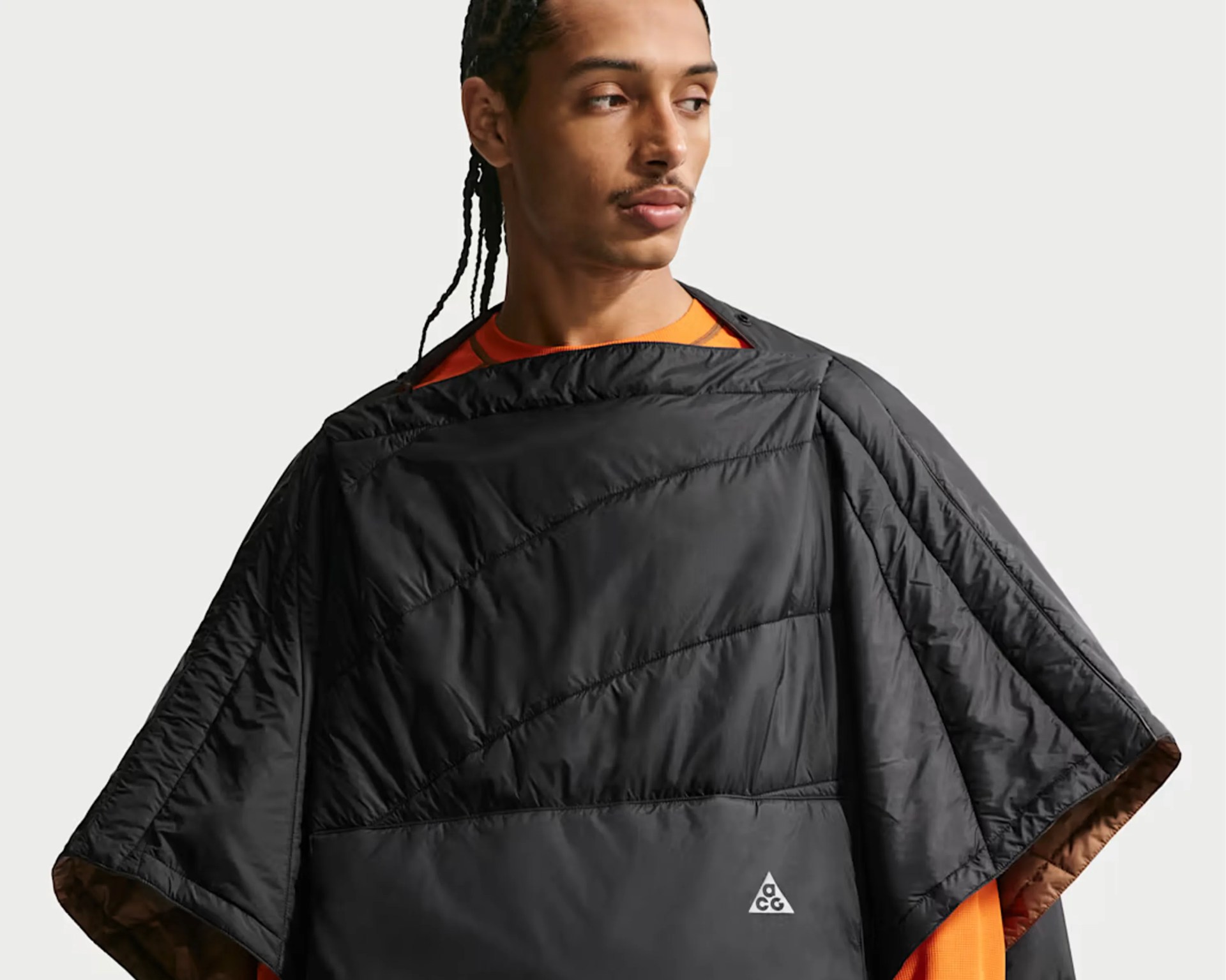 Black quilted poncho with ACG logo worn over an orange shirt.