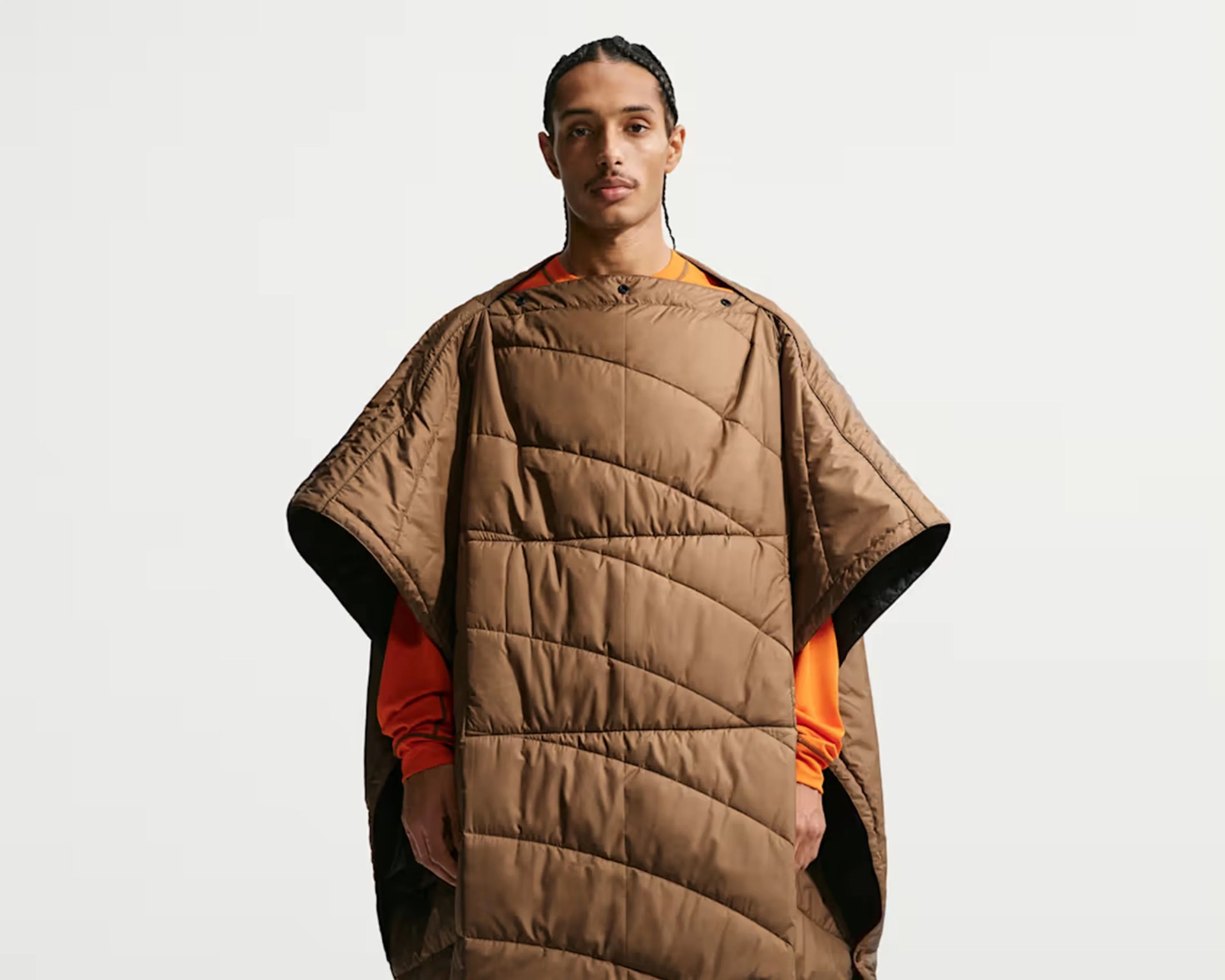 Brown quilted poncho with snap buttons worn over an orange long-sleeve shirt.