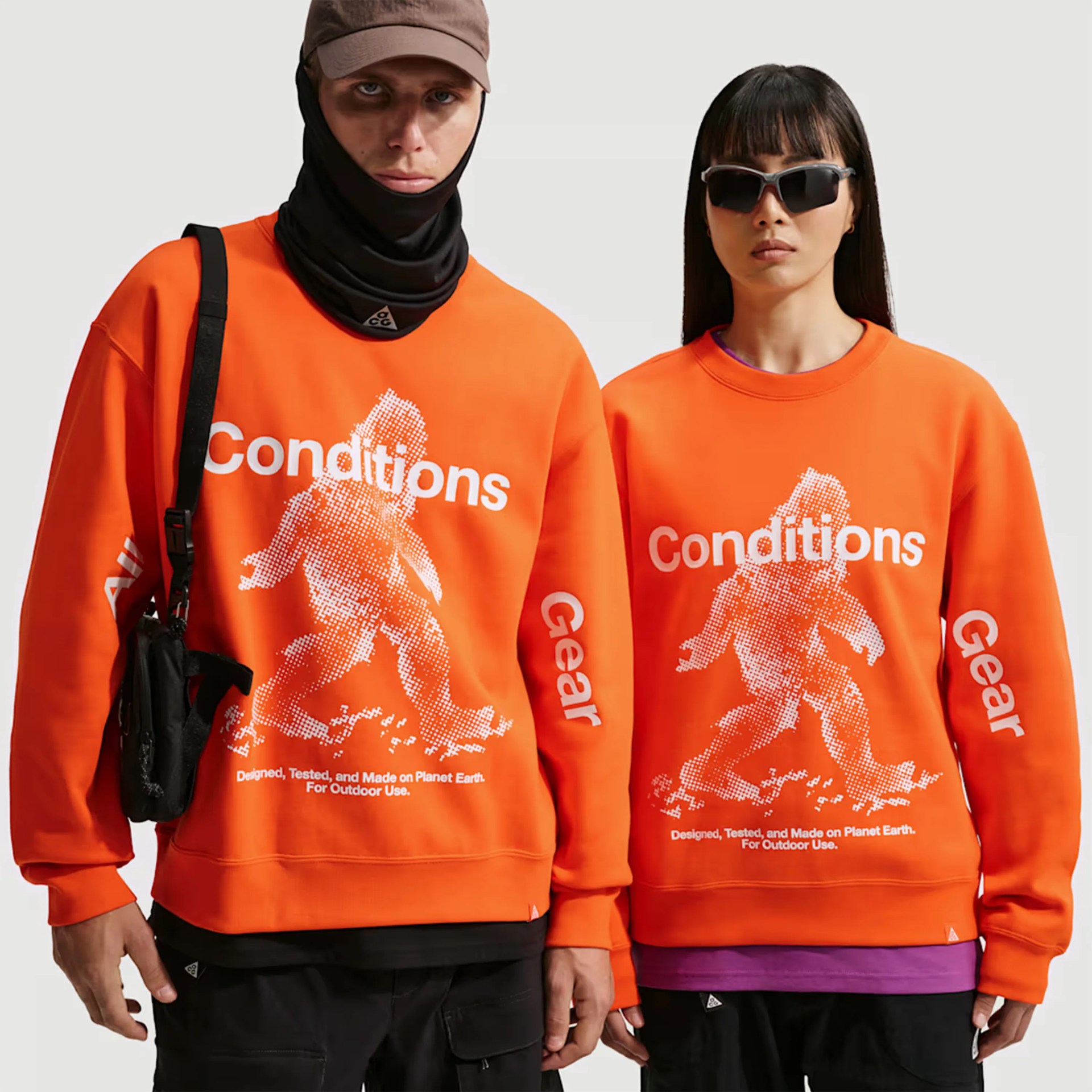 Two people wearing bright orange sweatshirts with white pixelated Bigfoot graphic and text "Conditions Gear" on front and sleeves.