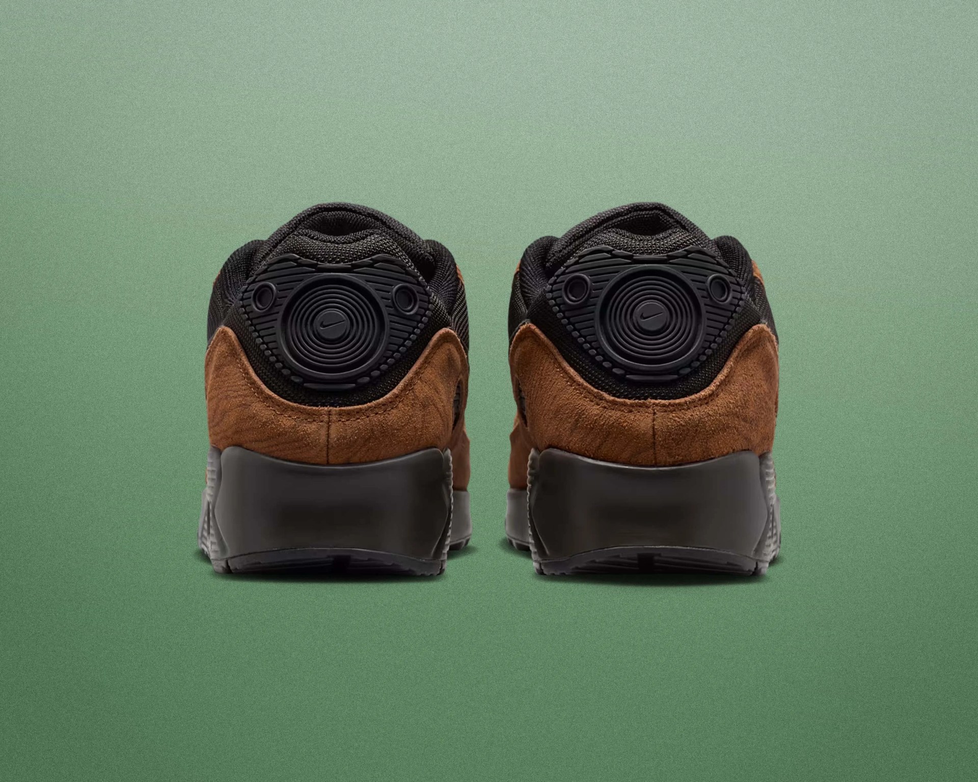Pair of brown suede and black Nike sneakers shown from the back on a green background.