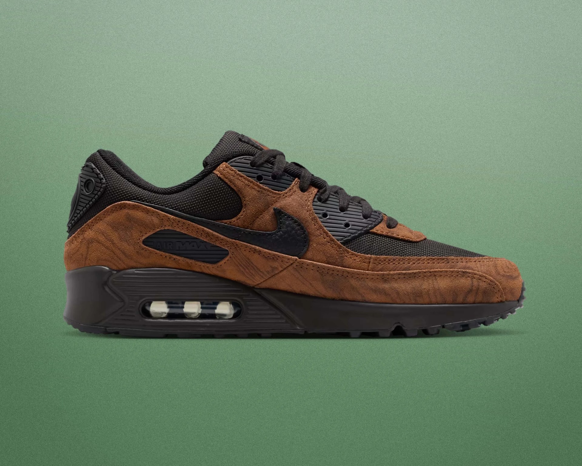 Brown suede and black mesh Nike Air Max sneaker with visible air sole unit on green background.