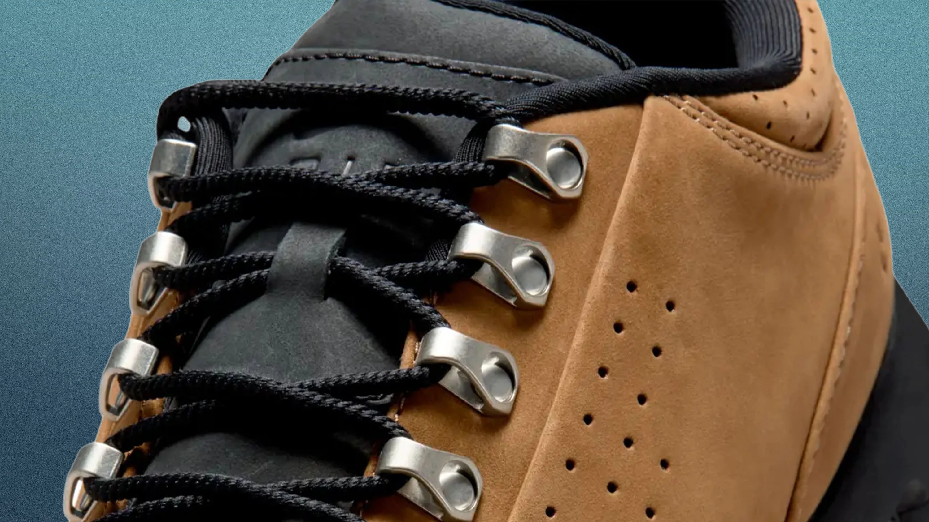 Close-up of a tan suede hiking boot with black laces threaded through silver metal eyelets.