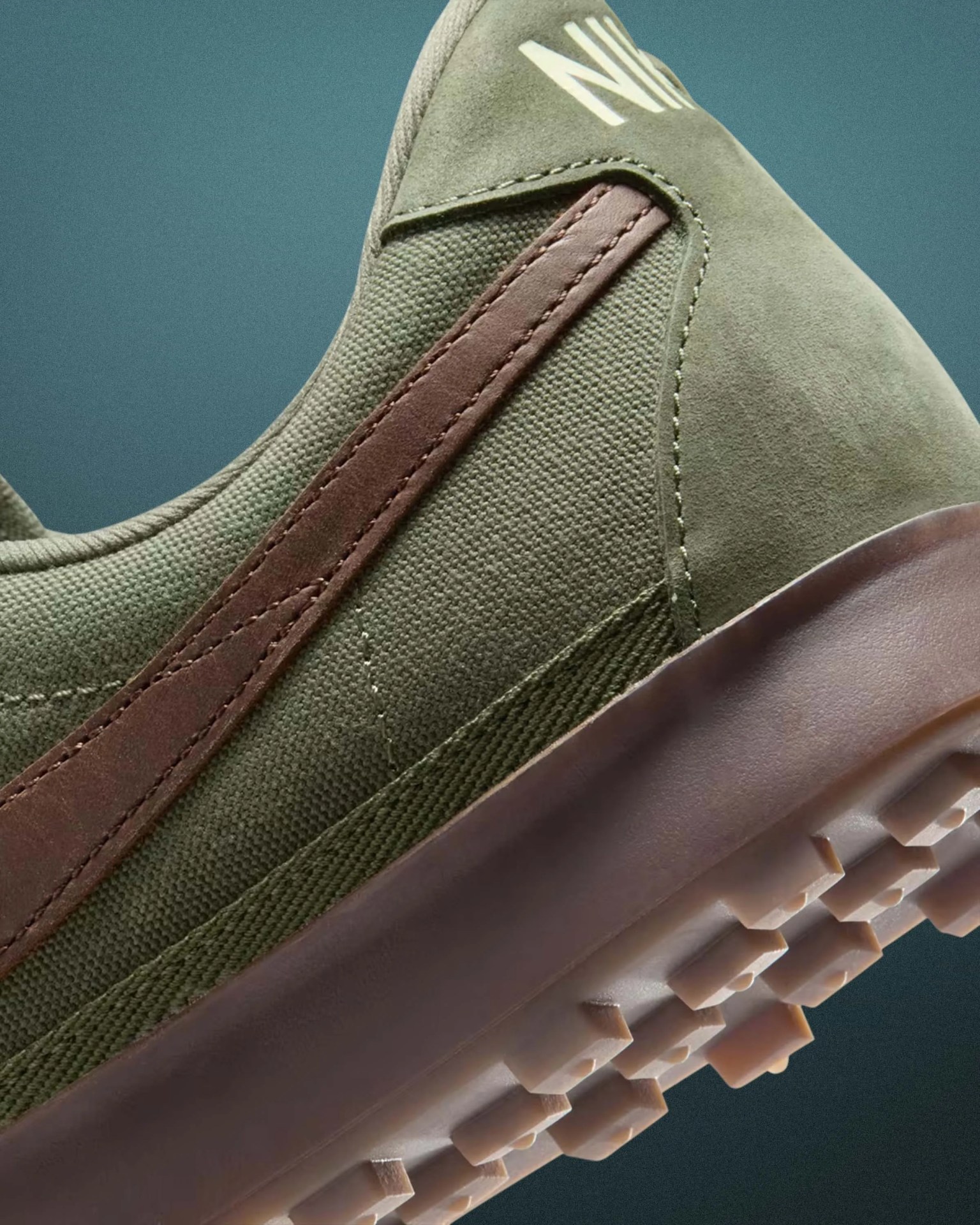 Close-up of olive green Nike sneaker with brown suede swoosh and textured rubber sole.