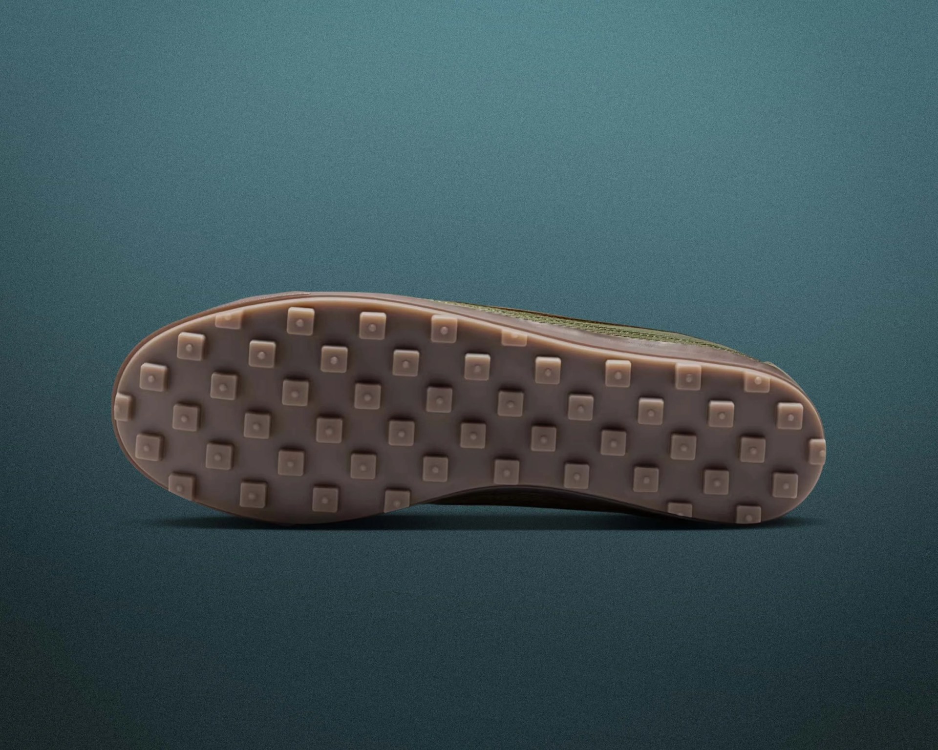 Brown rubber shoe sole with square-shaped treads on a teal background.