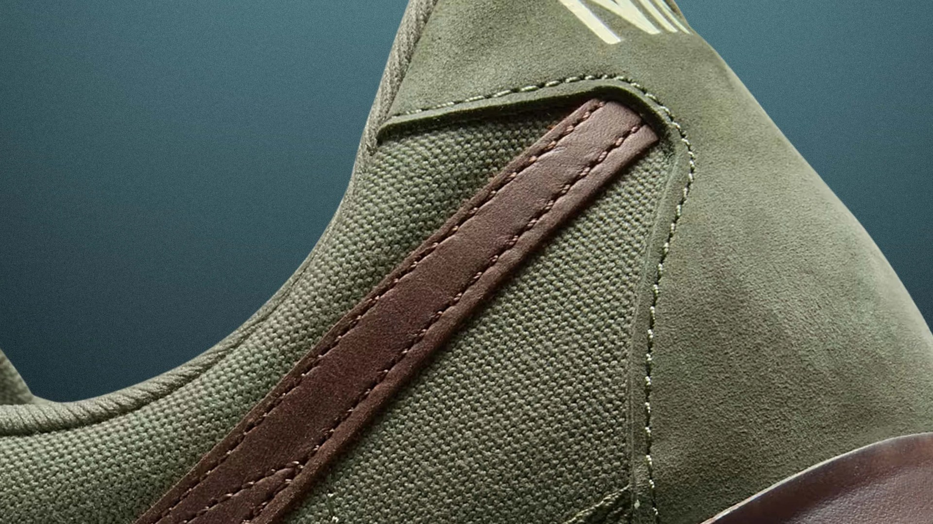 Close-up of an olive green sneaker with a textured fabric upper and a brown leather stripe detail.