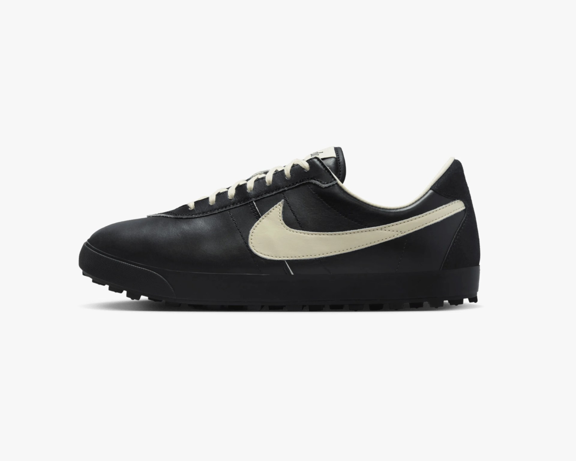 Black leather Nike sneaker with cream-colored swoosh and laces on a white background.