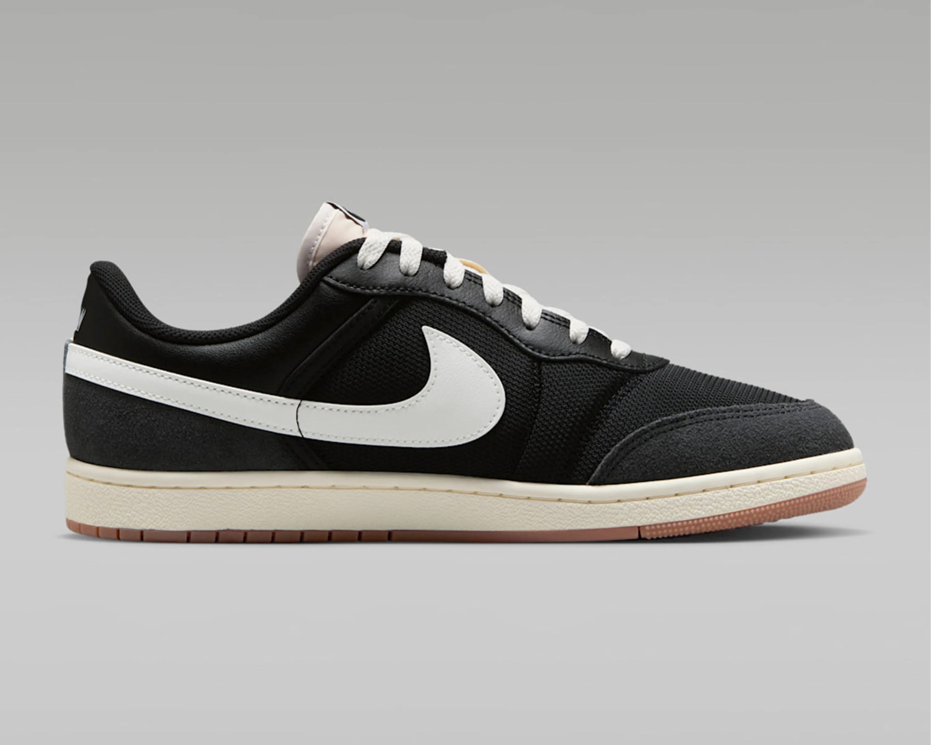 Black low-top Nike sneaker with white swoosh logo, white laces, and beige sole with gum outsole.