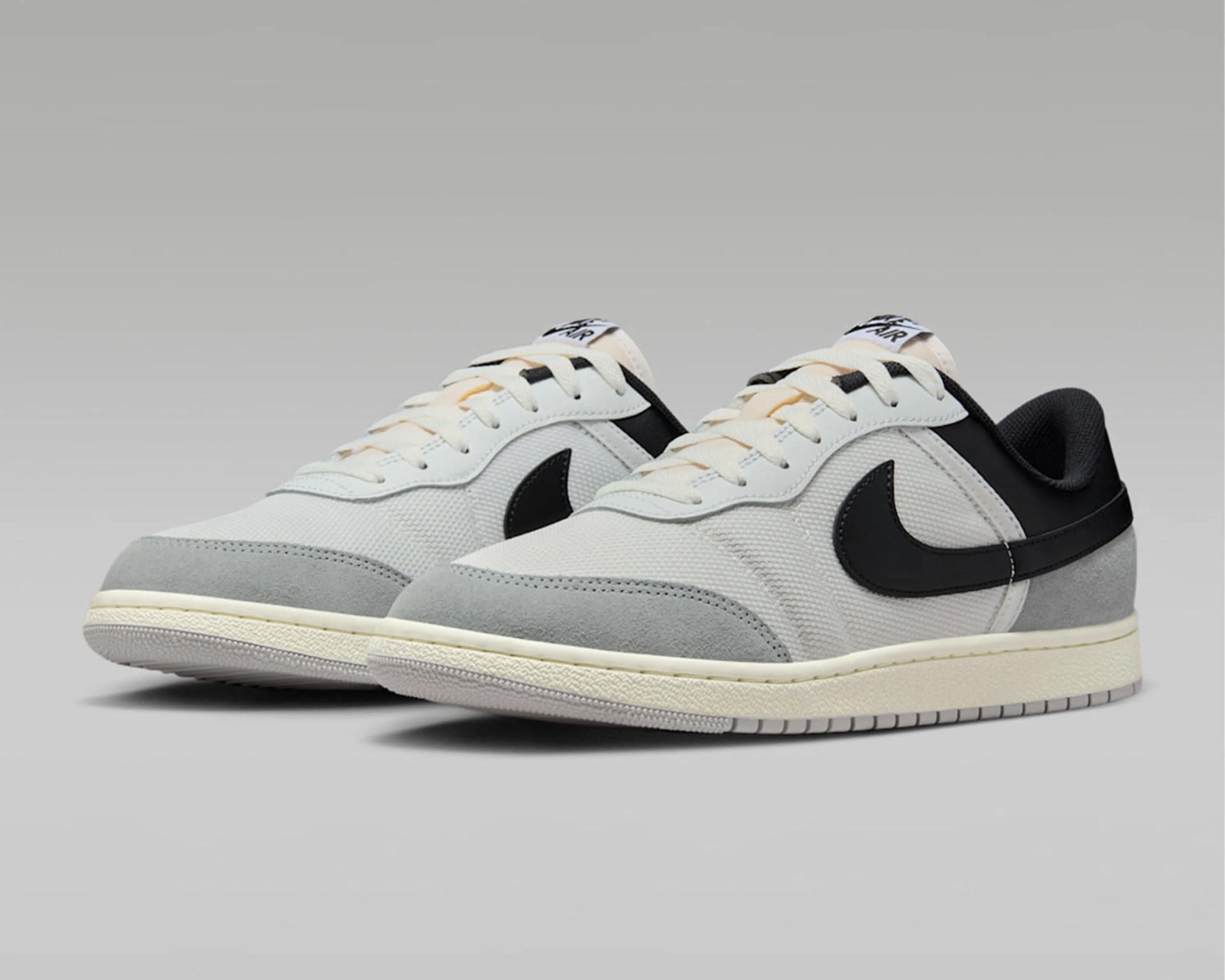 Pair of low-top Nike sneakers in white and light gray with black swoosh logos and cream-colored soles.